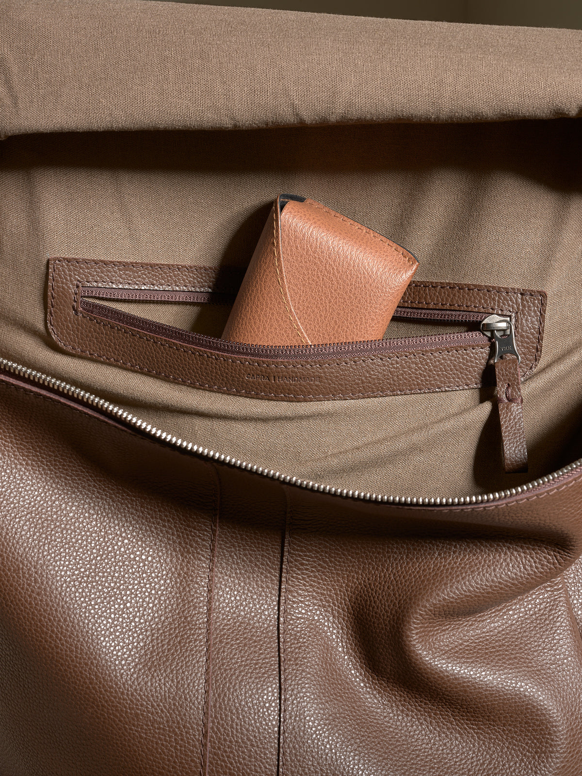 Interior shot of the Capra Leather backpack's lining with a zippered pocket holding a small leather wallet.
