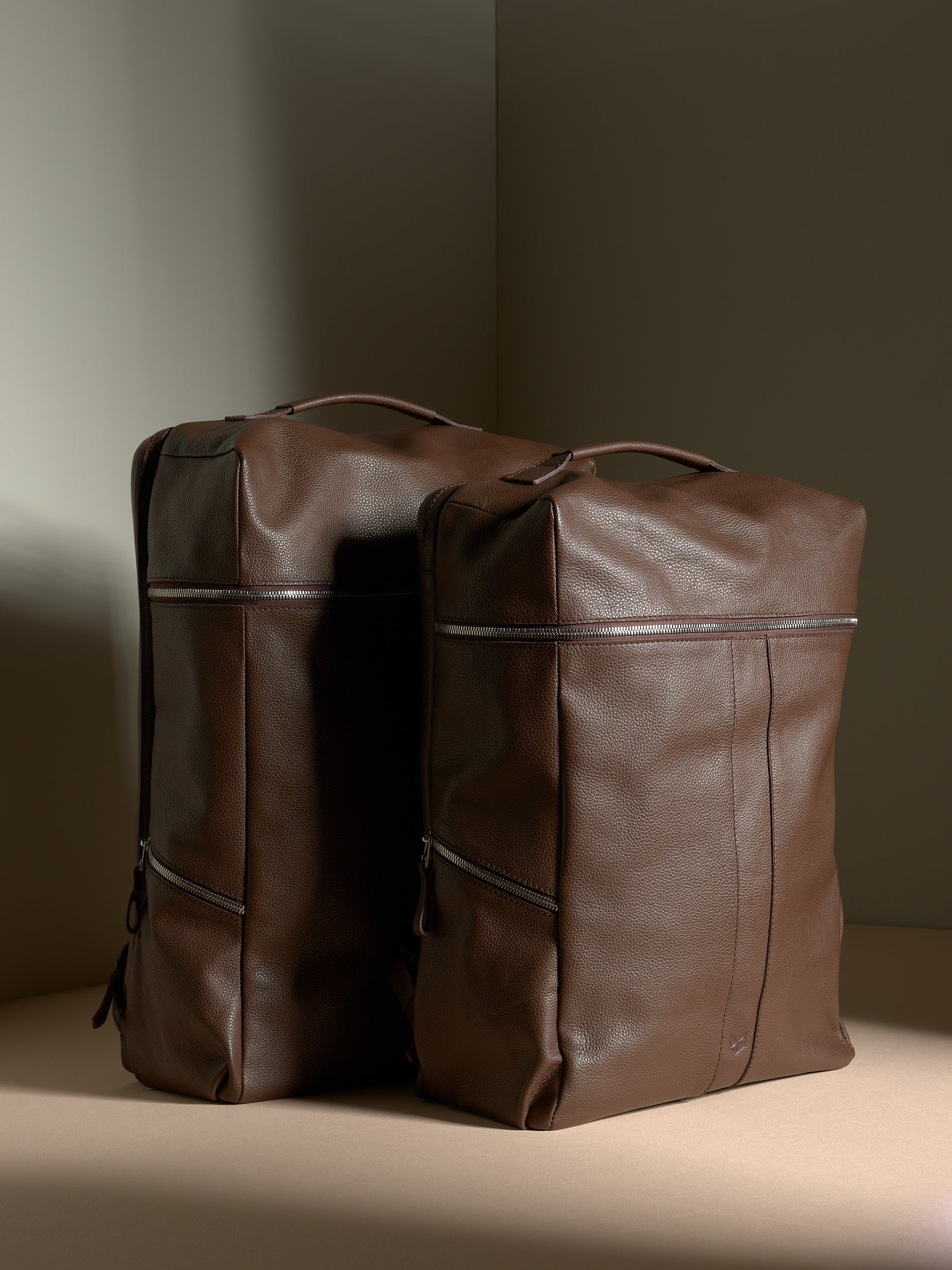 Two brown full-grain Capra Leather Banteng backpacks, showing large and small sizes, standing side-by-side.
