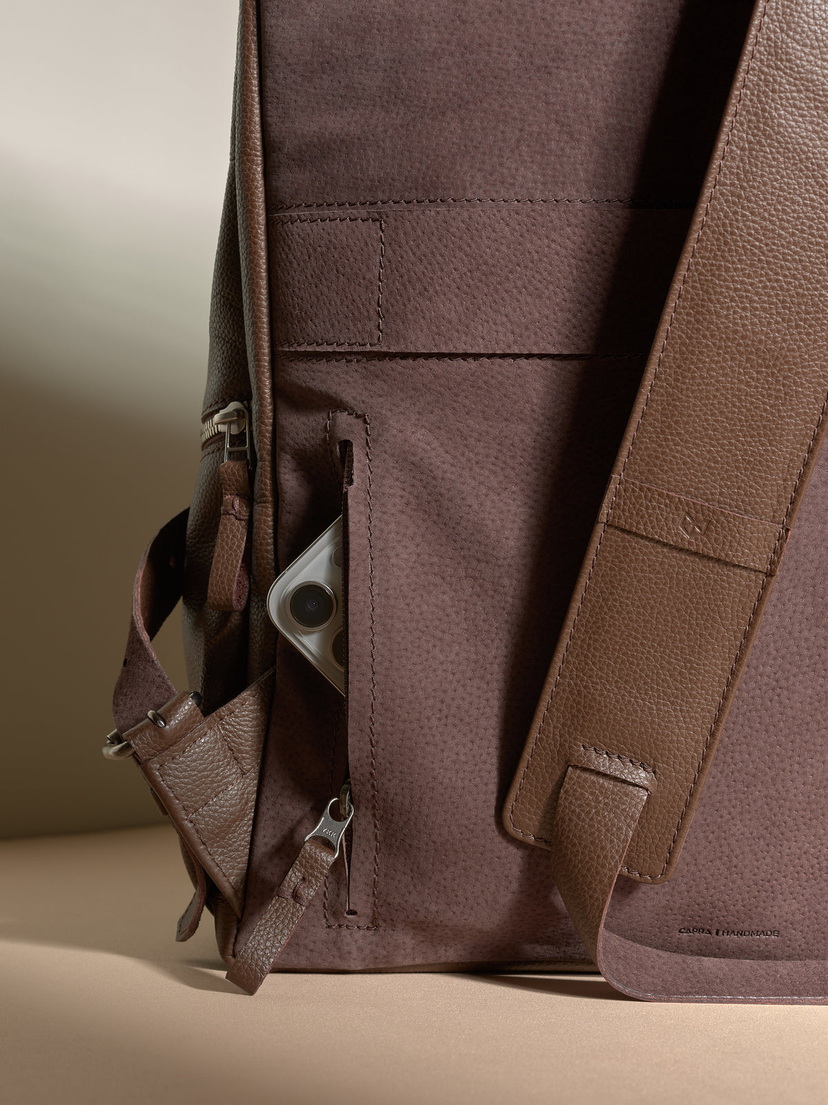 View of the brown leather backpack's hidden anti-theft pocket storing a silver-colored smartphone.