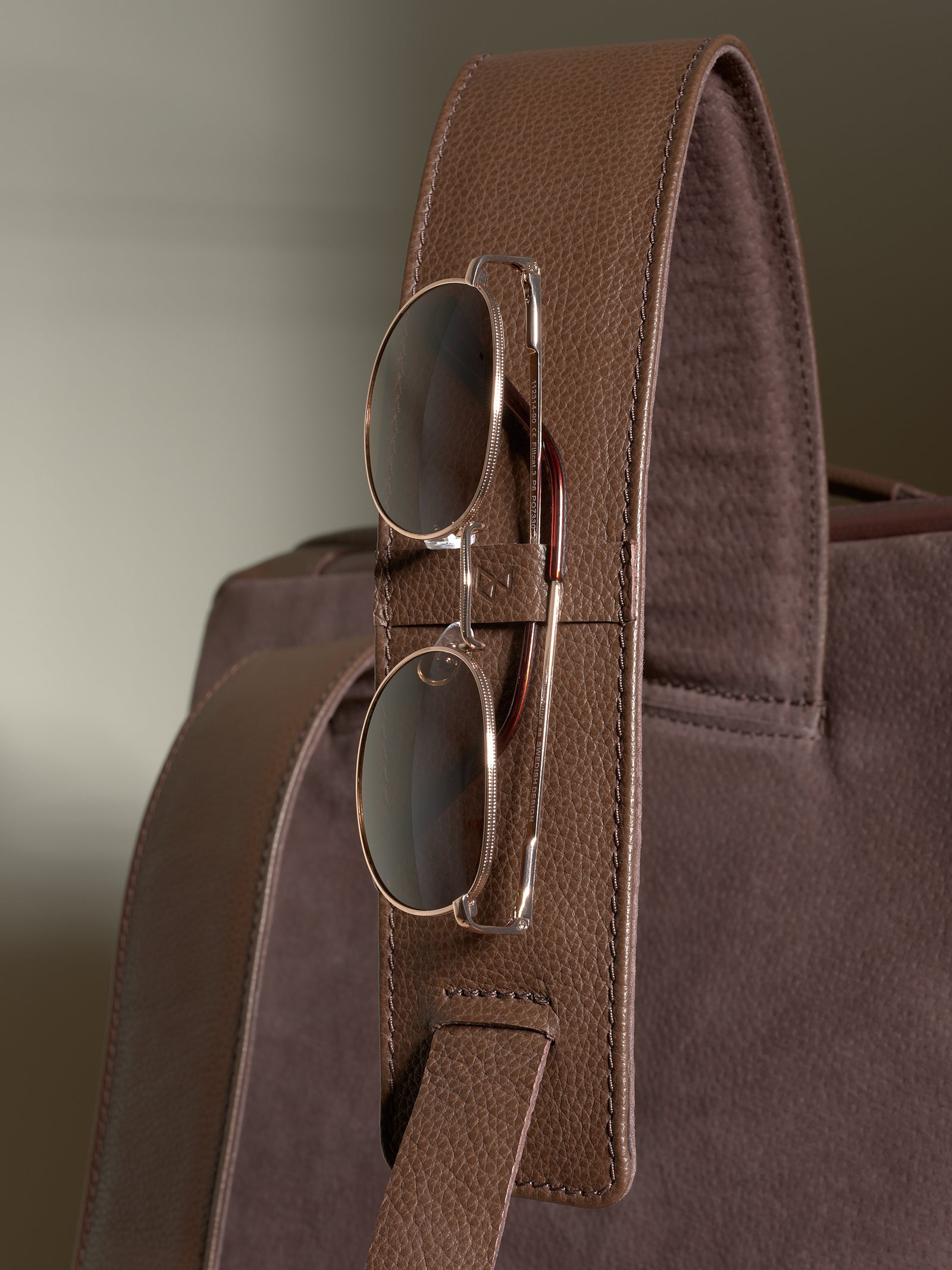 Close-up of the leather shoulder strap with a dedicated loop holding a pair of aviator sunglasses.
