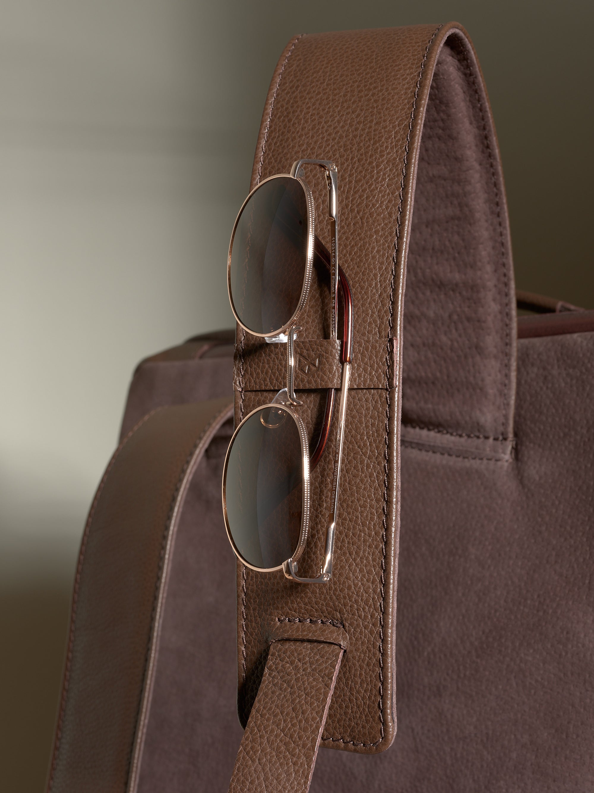 Close-up of the leather shoulder strap with a dedicated loop holding a pair of aviator sunglasses.
