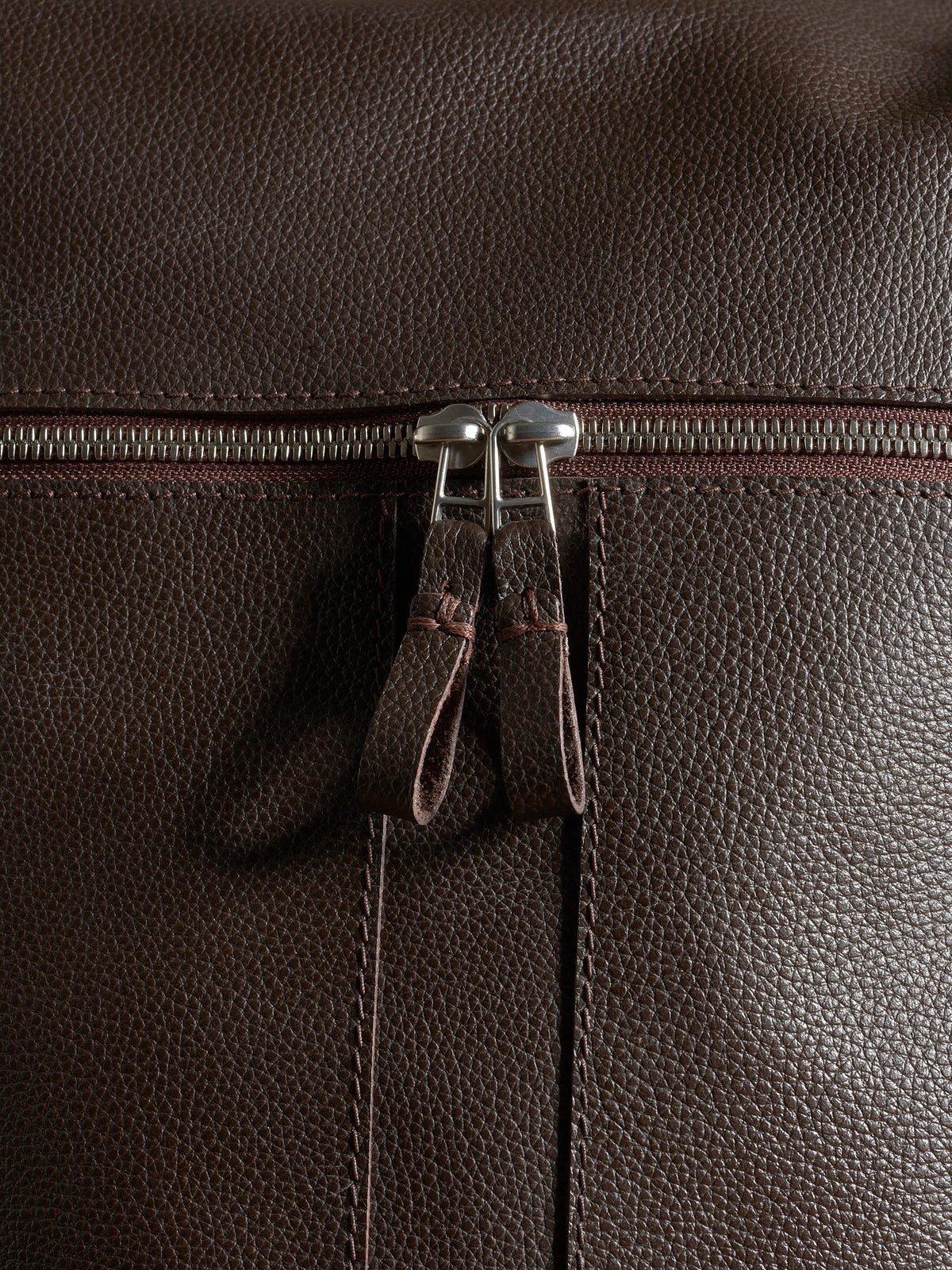 Close-up of premium pebbled dark brown leather texture and durable silver zipper hardware.