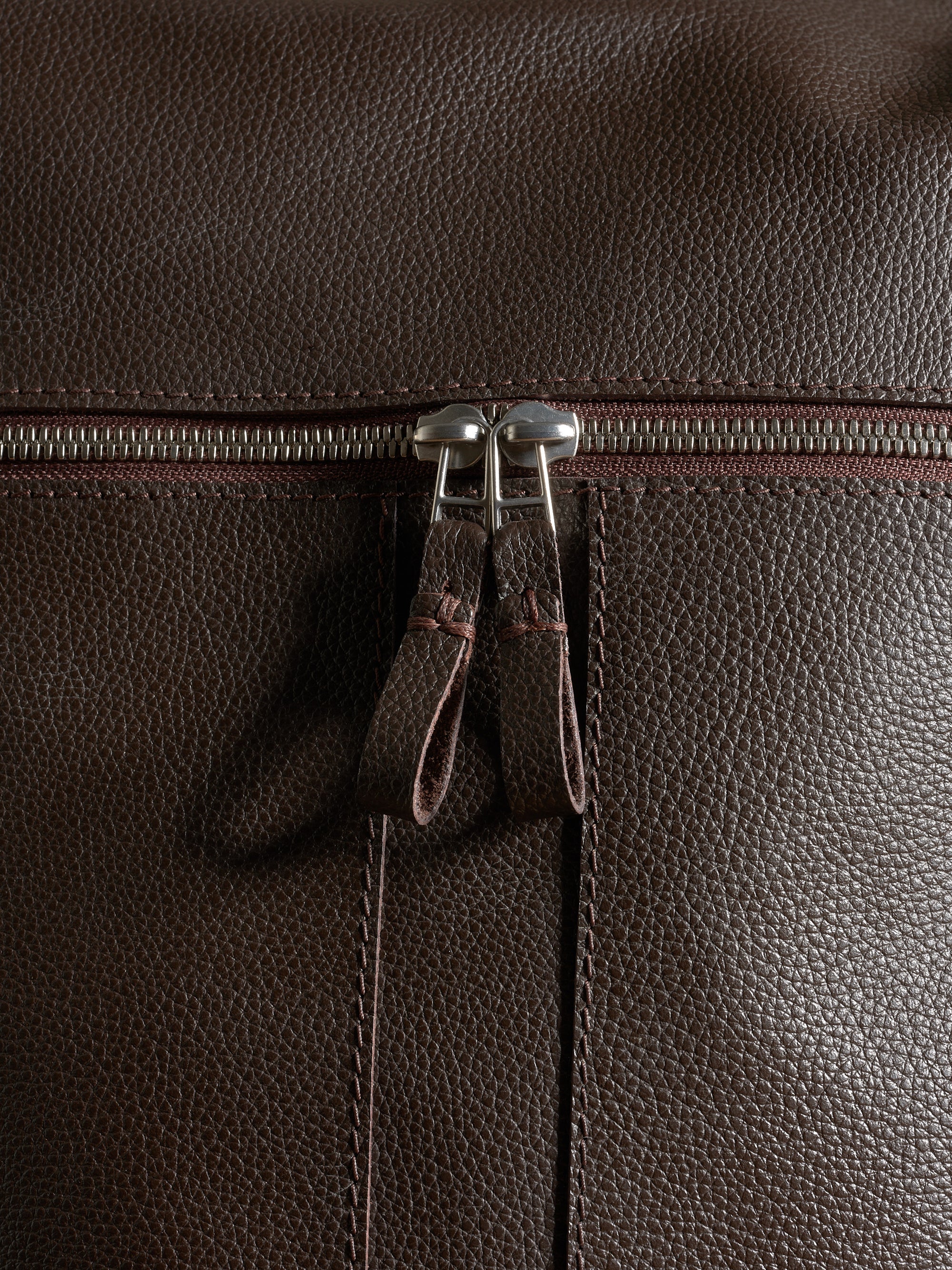 Close-up of premium pebbled dark brown leather texture and durable silver zipper hardware.