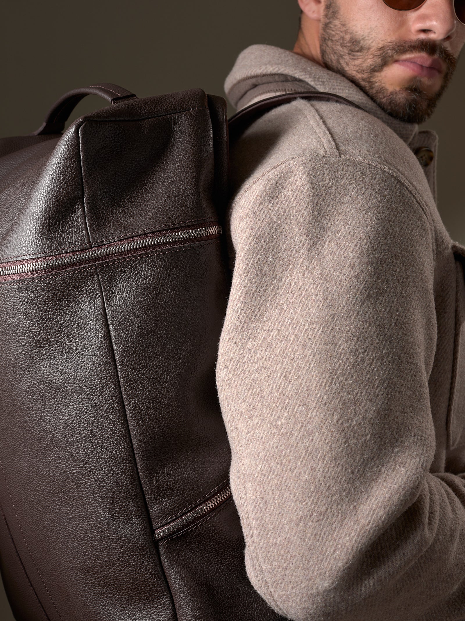 Close-up of a man wearing the Dark Brown Capra Banteng Leather Backpack over a light wool coat.