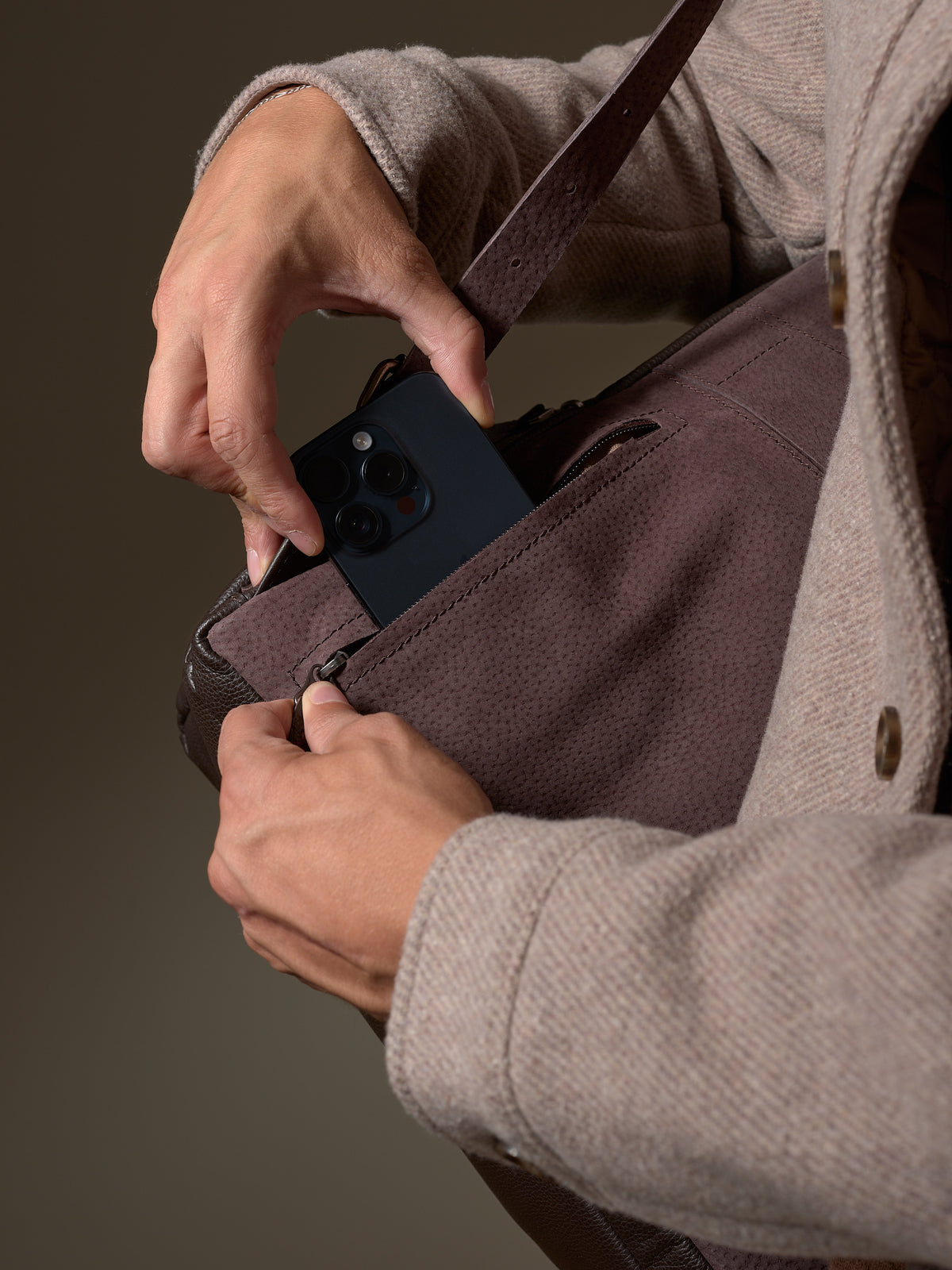 Hand putting phone into the side pocket of the Dark Brown Leather Banteng Backpack.