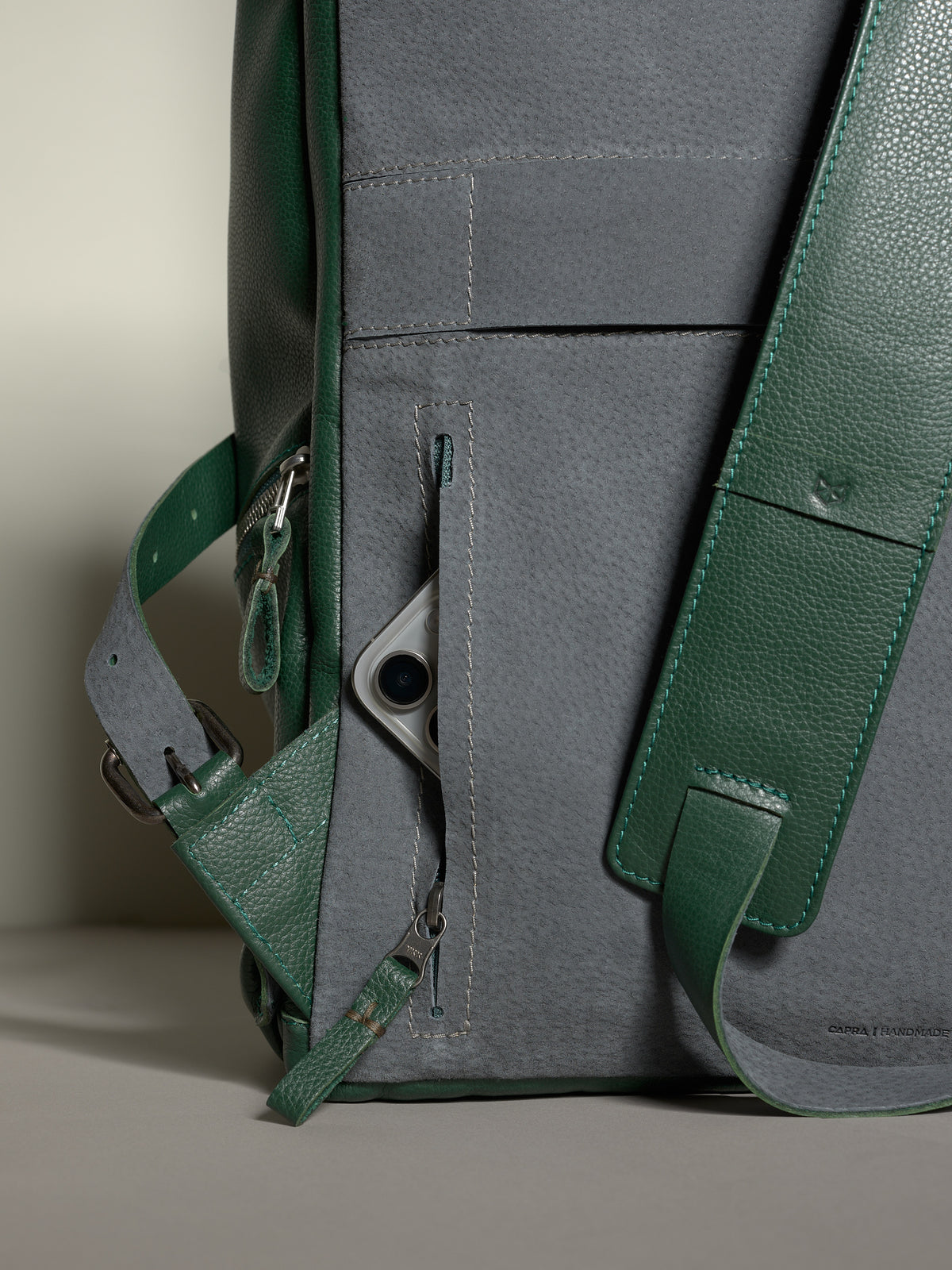 Back panel of the Capra Banteng leather backpack in green and gray with a hidden pocket storing a cell phone.