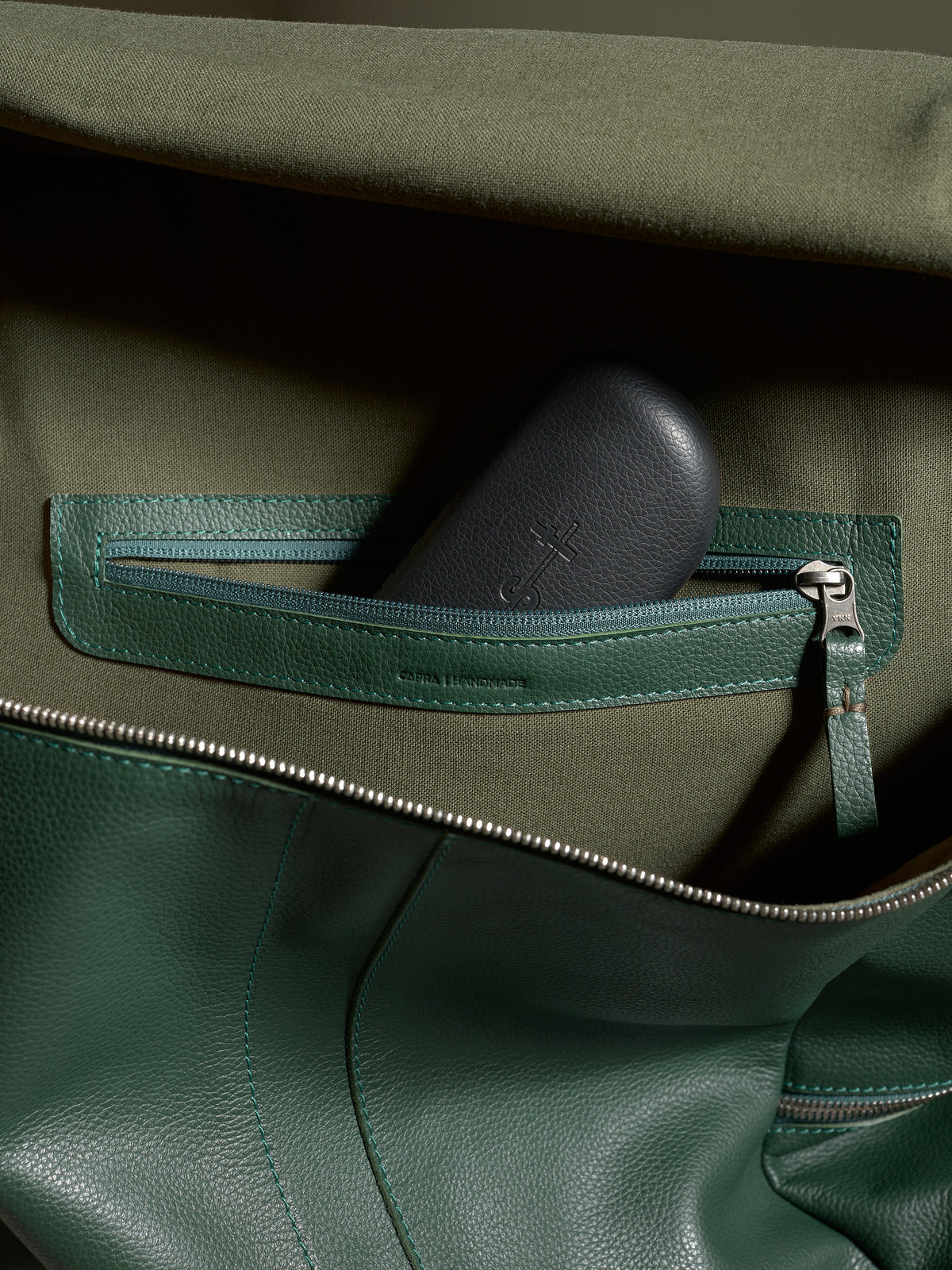 Interior view of the green leather Capra Banteng backpack with a zippered pocket and dark accessory case.