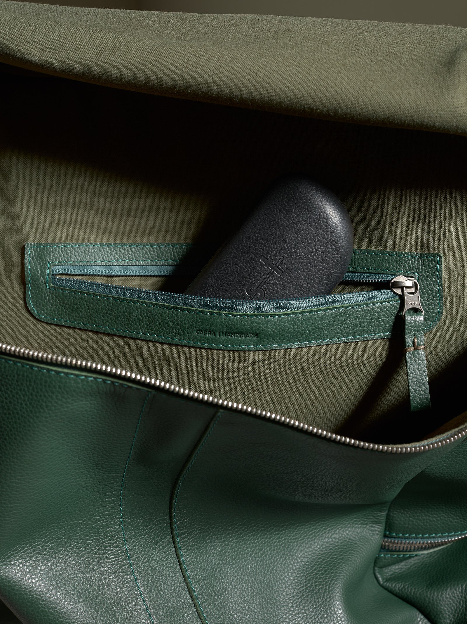 Interior view of the green leather Capra Banteng backpack with a zippered pocket and dark accessory case.