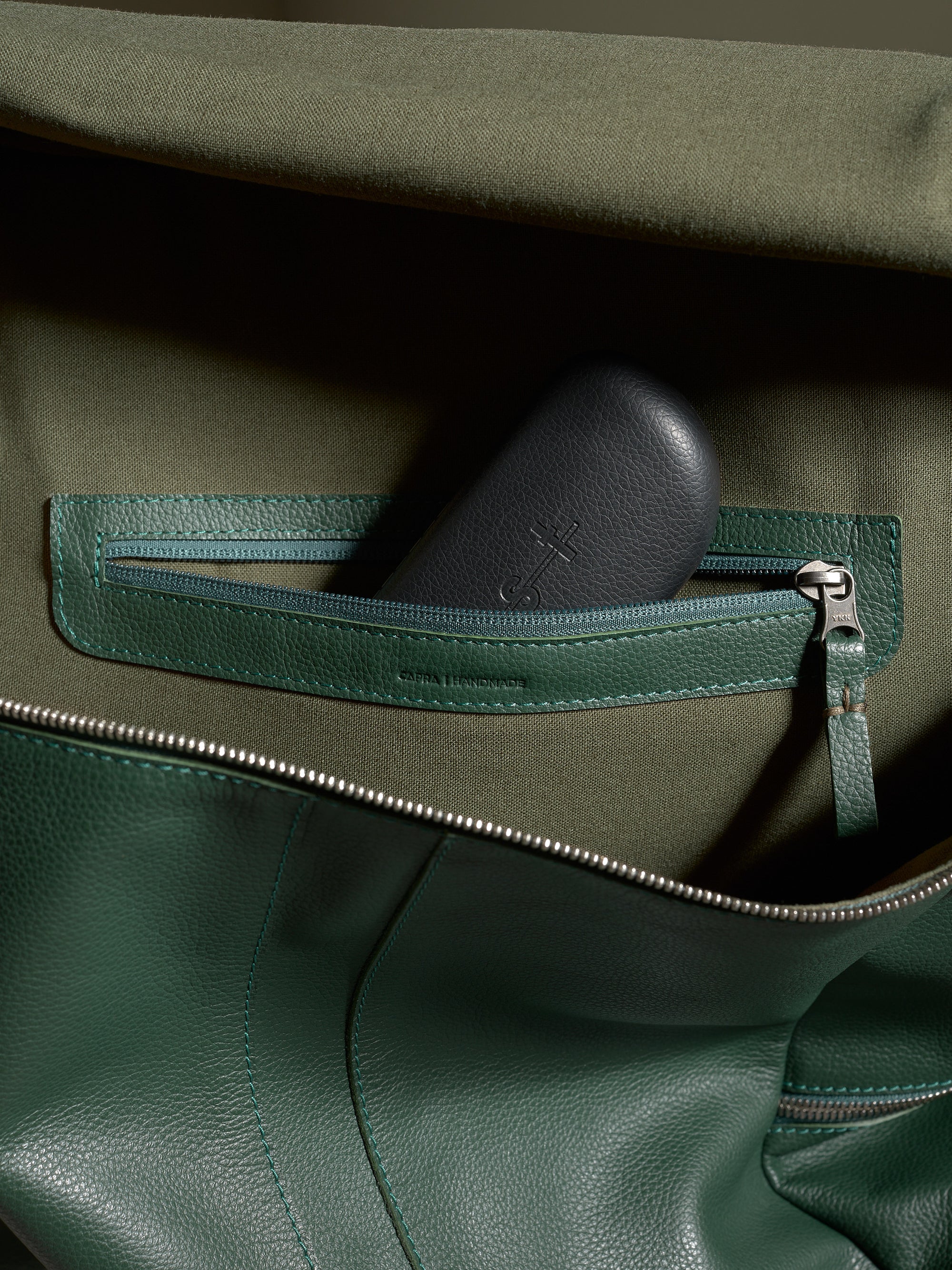 Interior view of the green leather Capra Banteng backpack with a zippered pocket and dark accessory case.