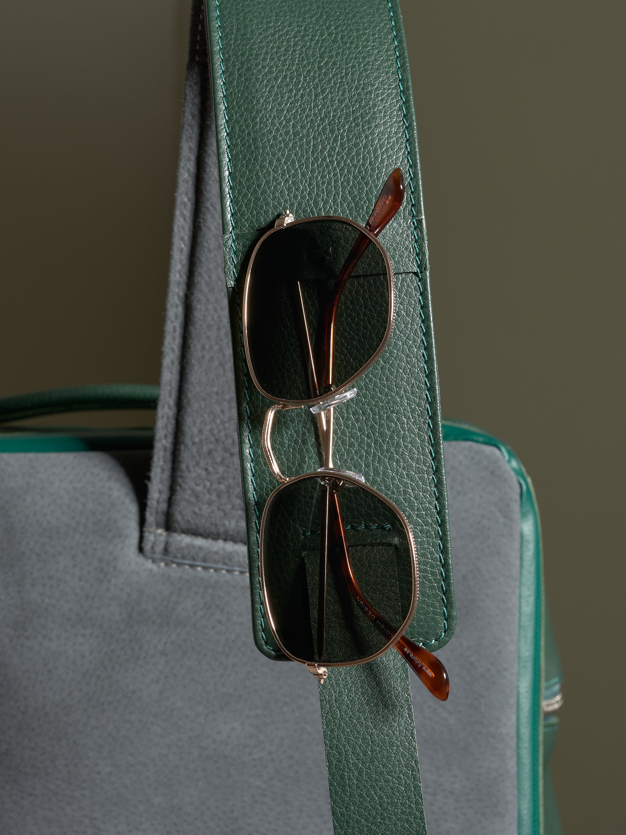 Green leather shoulder strap detail on the Banteng backpack, featuring a functional loop holding a pair of sunglasses.