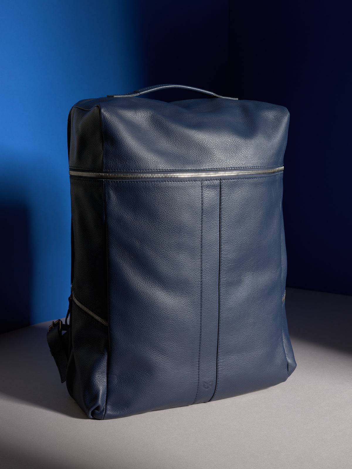 A three-quarter view of the Banteng men&#39;s backpack in navy blue pebbled leather, showing its minimalist front panel.