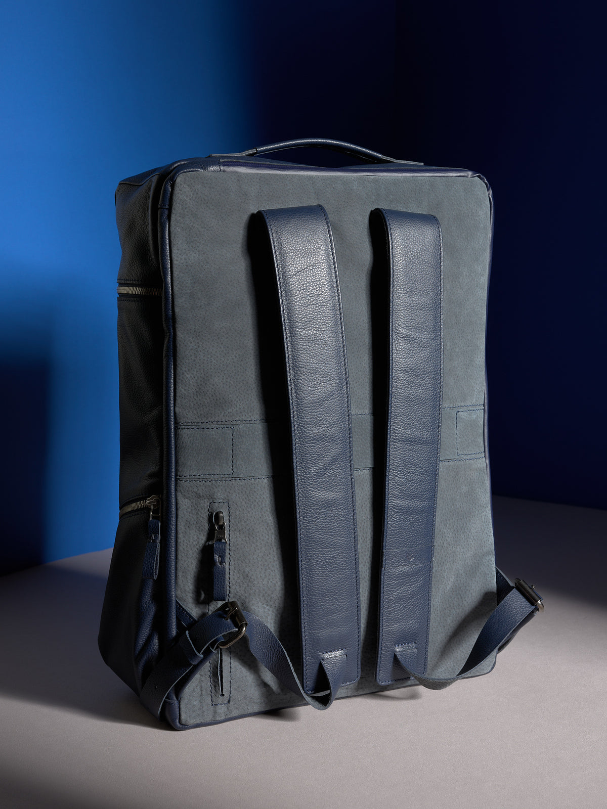 The back of the navy leather Banteng backpack, featuring comfortable padded shoulder straps and a grey suede back panel.