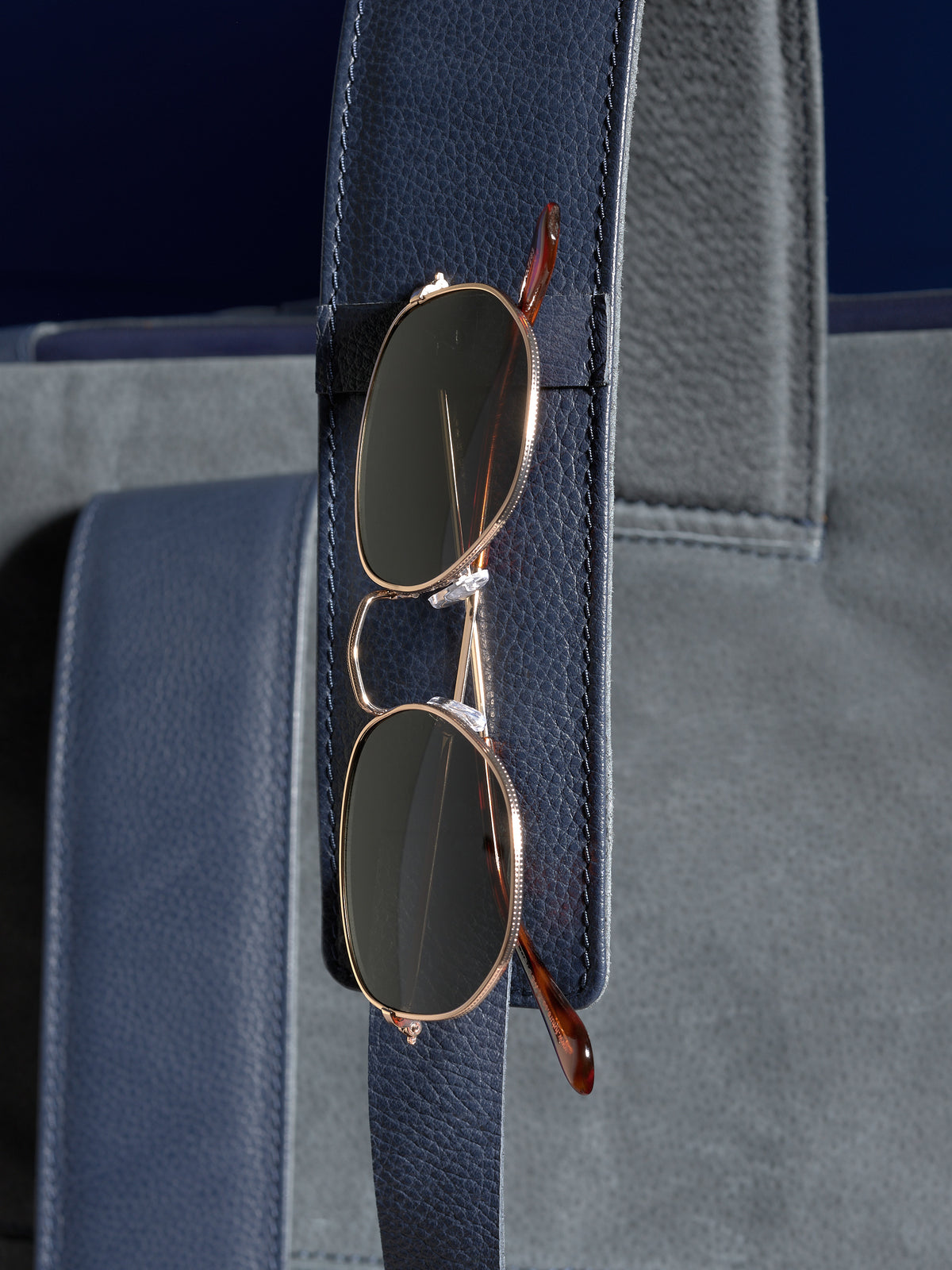 A pair of sunglasses neatly held in the dedicated leather loop on the shoulder strap of the Banteng navy backpack.