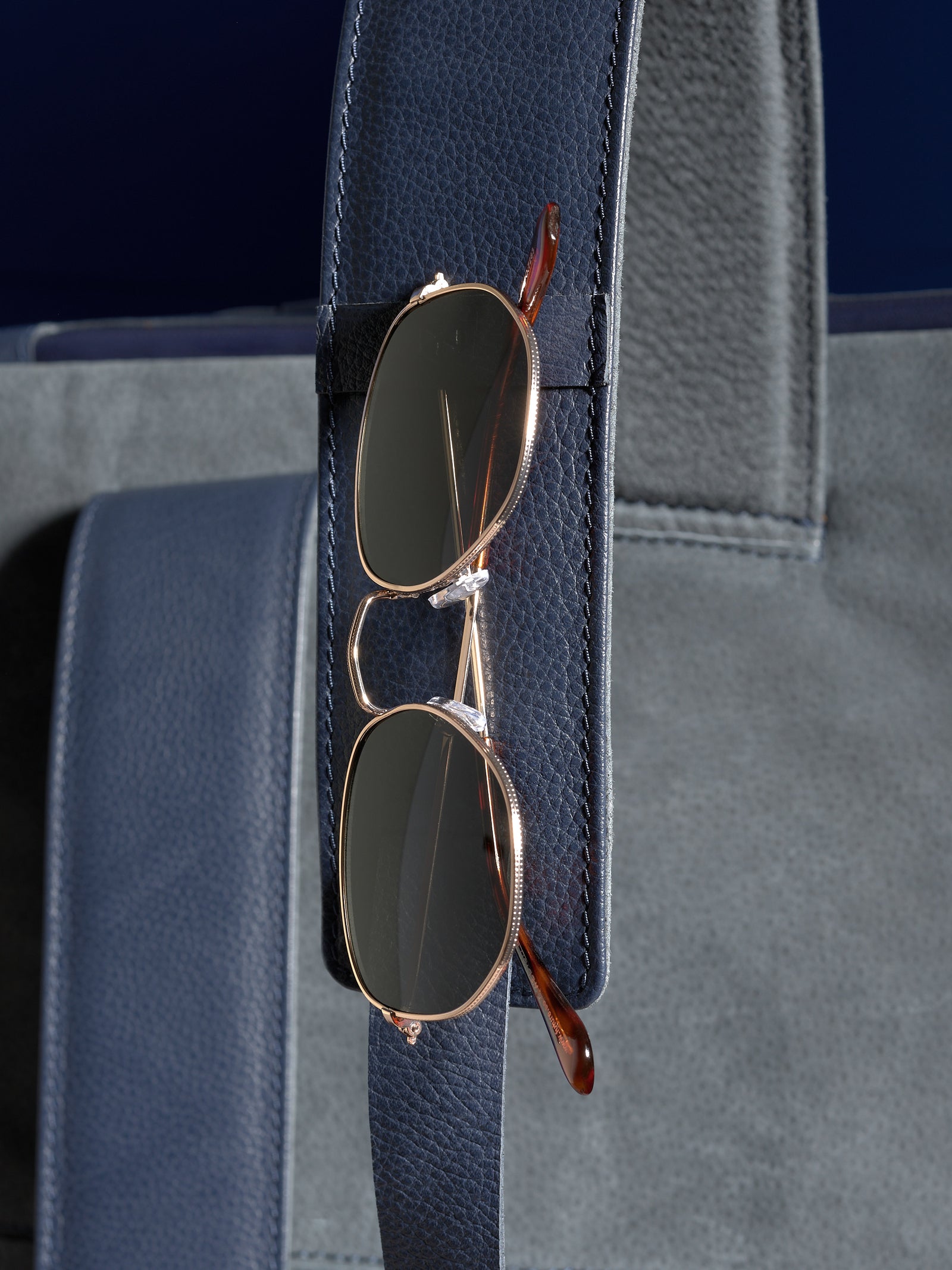 A pair of sunglasses neatly held in the dedicated leather loop on the shoulder strap of the Banteng navy backpack.