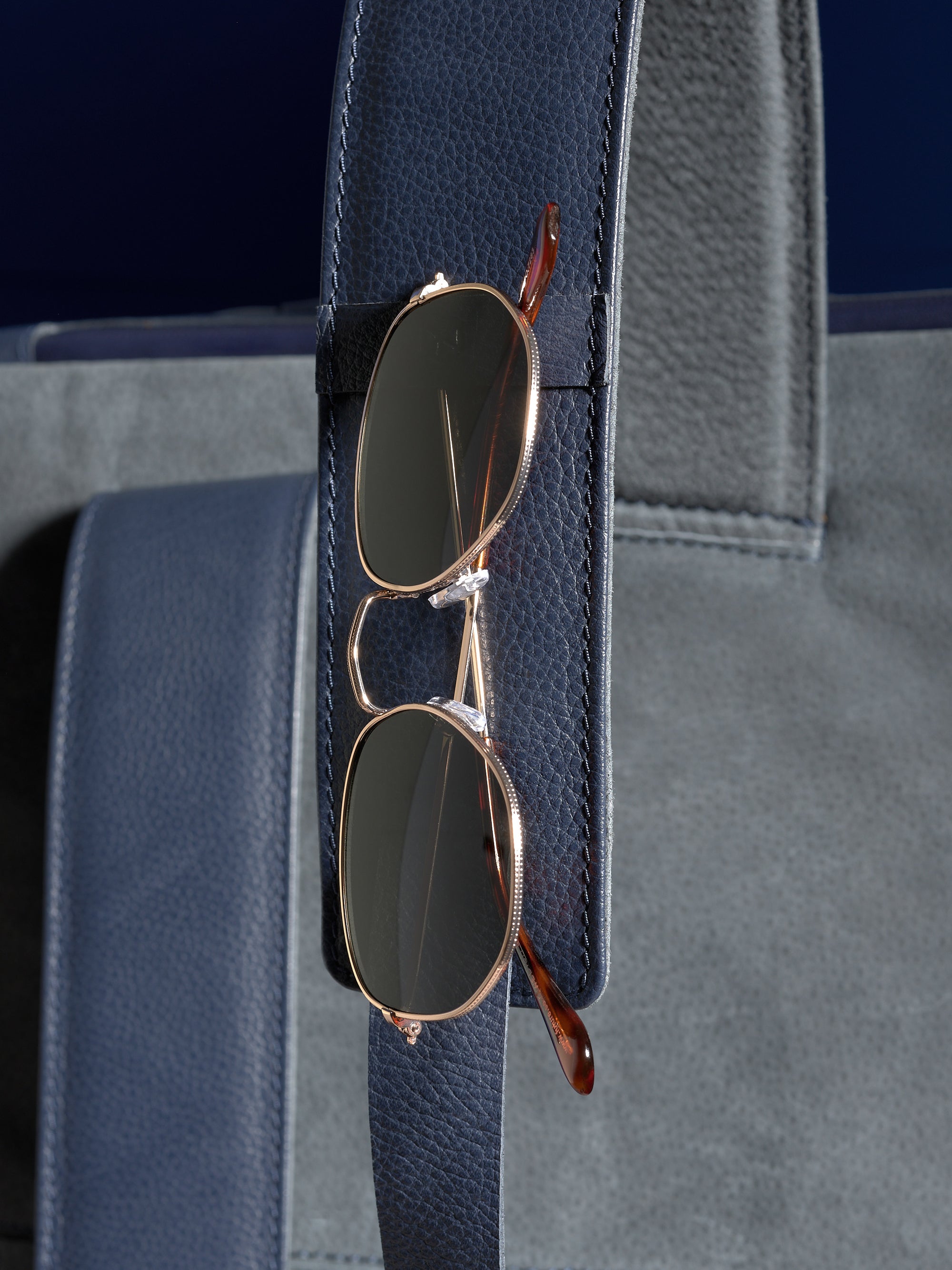 A pair of sunglasses neatly held in the dedicated leather loop on the shoulder strap of the Banteng navy backpack.