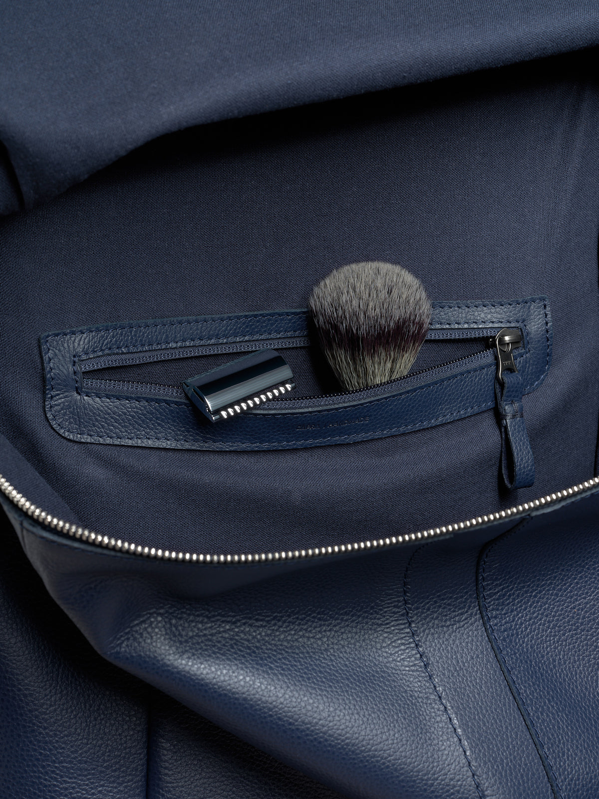 An interior zippered pocket of the Banteng backpack holding a razor and shaving brush, showcasing its travel utility.