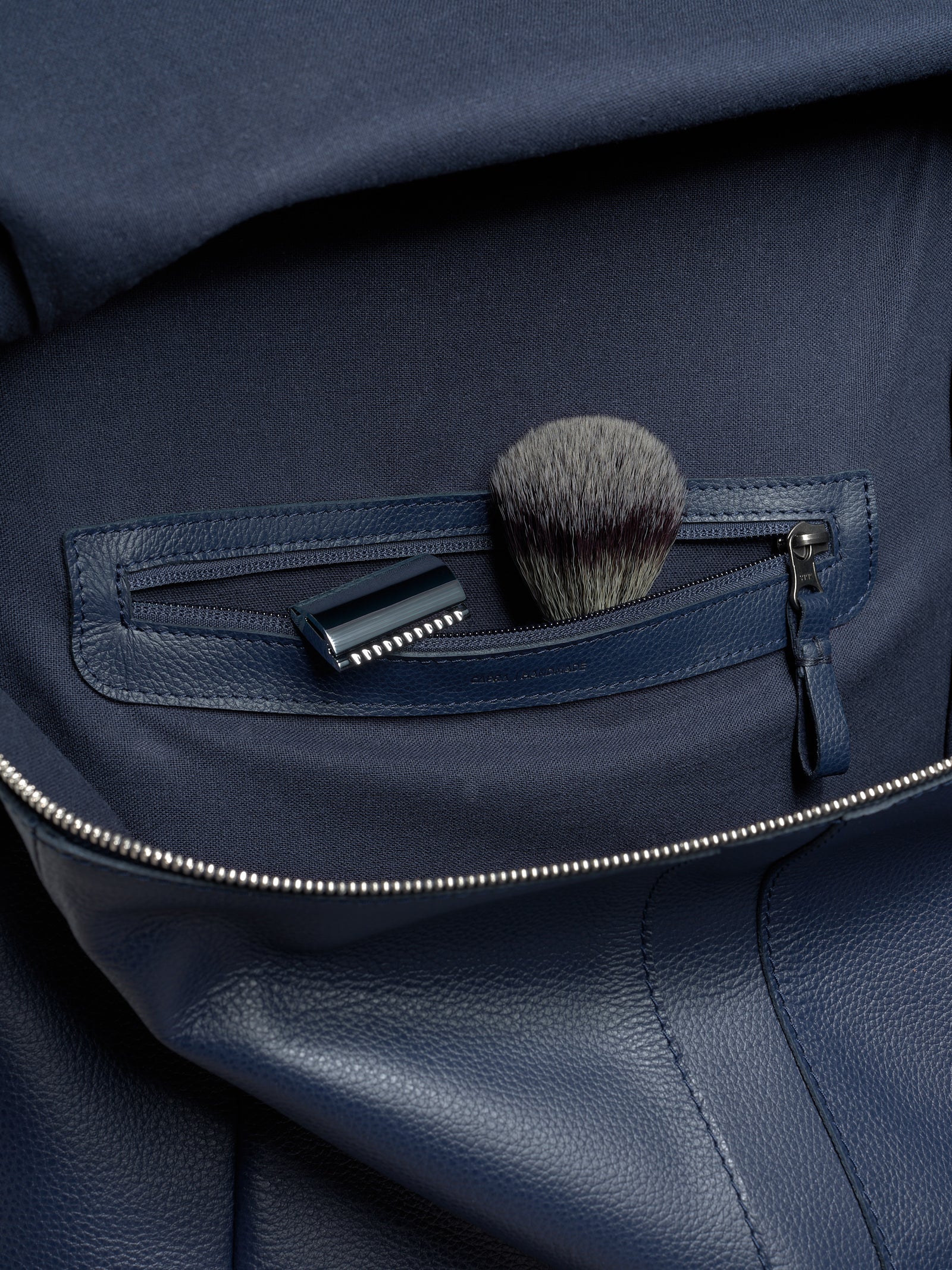 An interior zippered pocket of the Banteng backpack holding a razor and shaving brush, showcasing its travel utility.