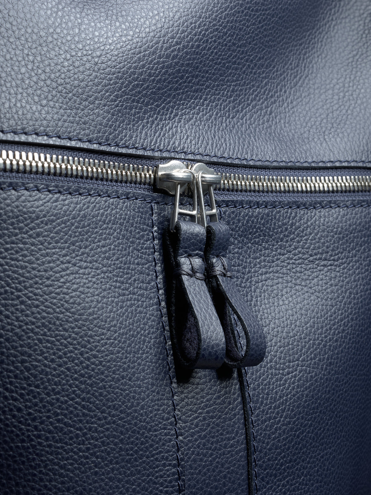 A macro shot of the durable silver-tone zipper and dual navy leather pulls on the Banteng backpack.