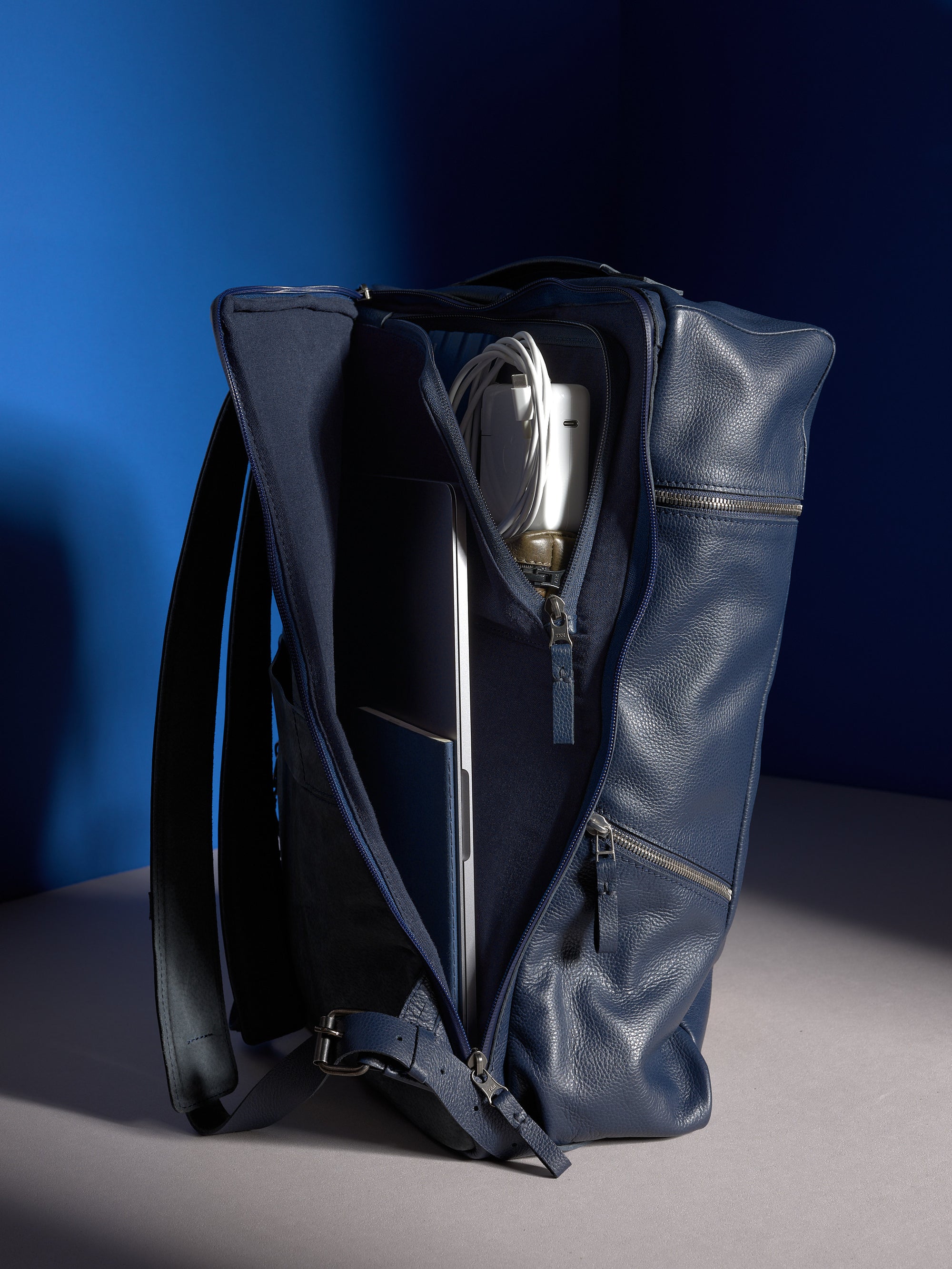 A three-quarter view of the Banteng men's backpack in navy blue pebbled leather, showing its minimalist front panel.