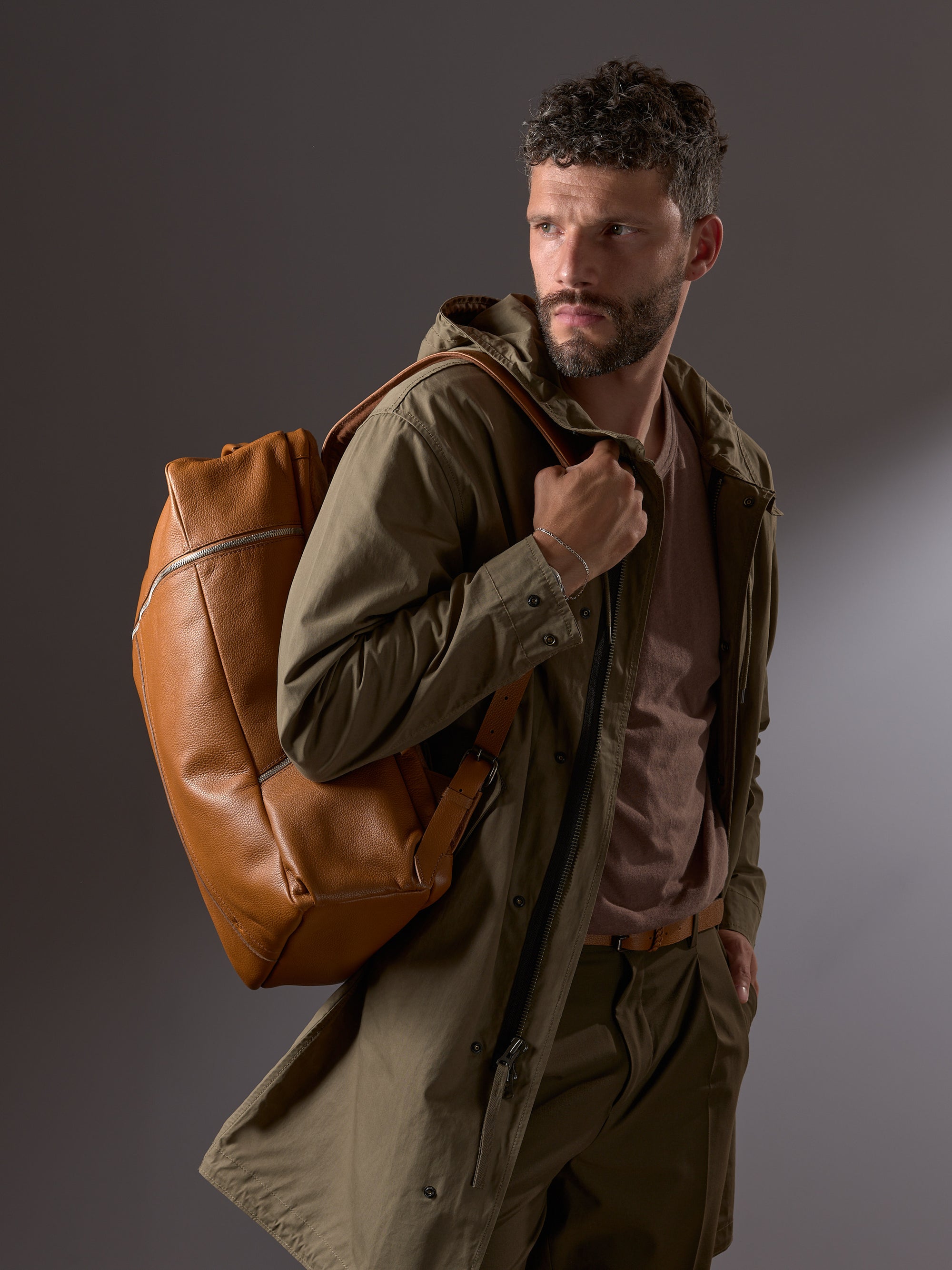 Stylish man wearing the tan leather Capra Banteng backpack over an olive green jacket, looking sharp.