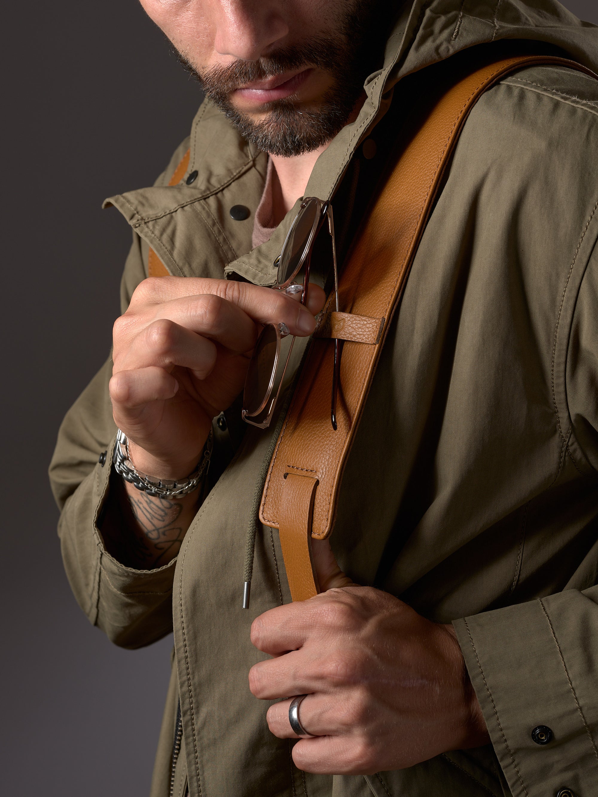 Close-up of a hand adjusting the durable tan leather shoulder strap of the Capra Banteng backpack.