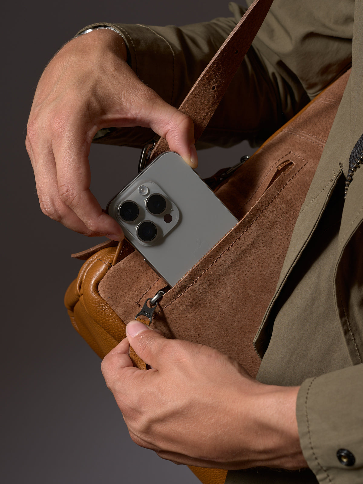 Man holding the Capra Tan Leather Backpack by the handle, showcasing its size and rich color.