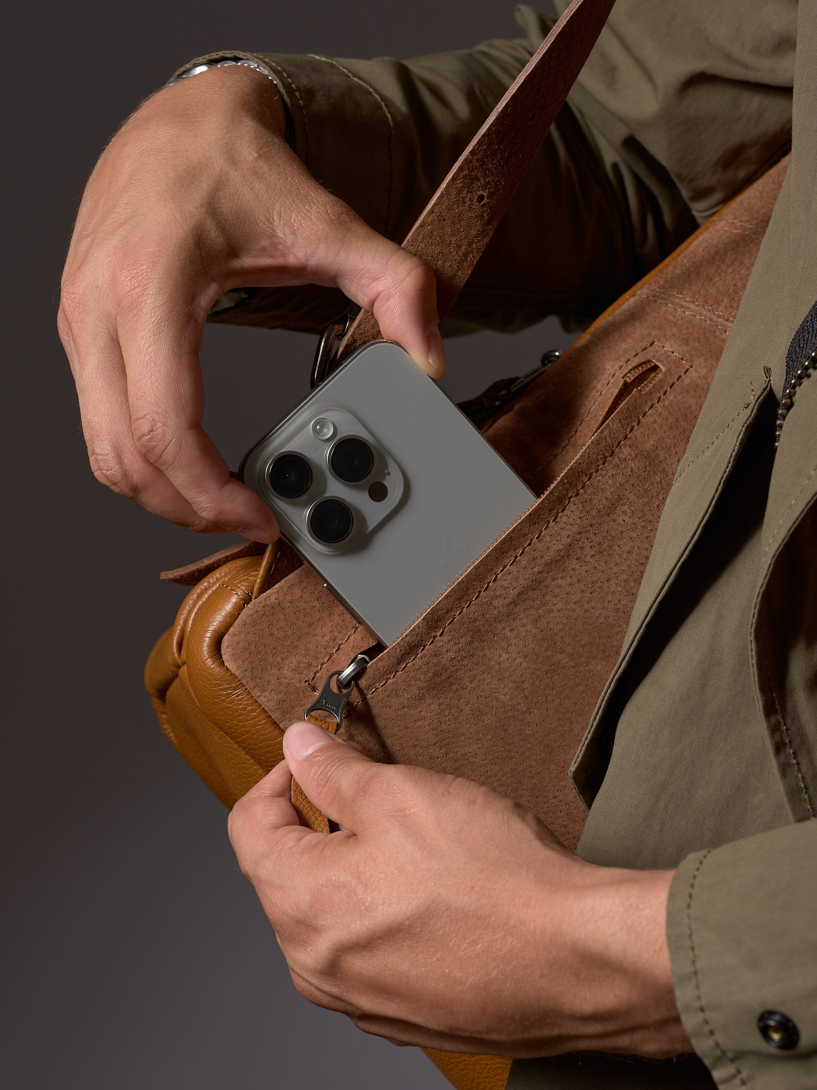 Man holding the Capra Tan Leather Backpack by the handle, showcasing its size and rich color.