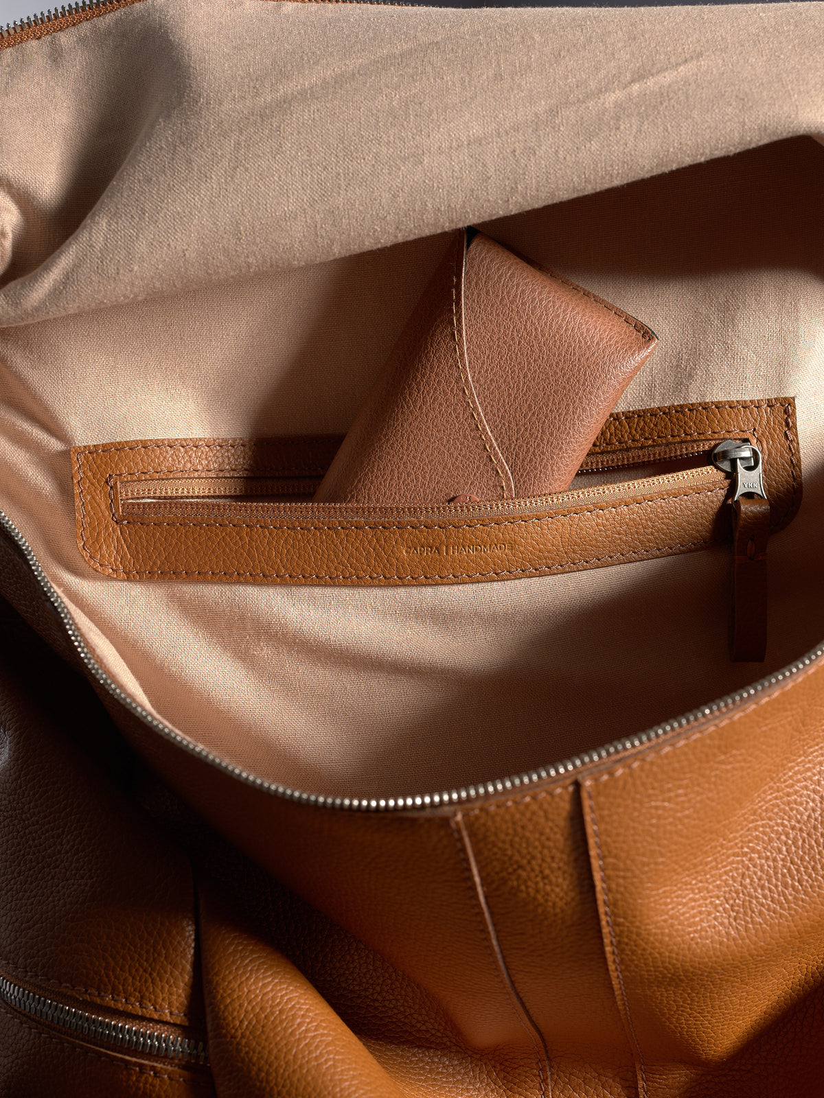 Interior shot of the Capra backpack showing a small leather accessory tucked into a zippered pocket.