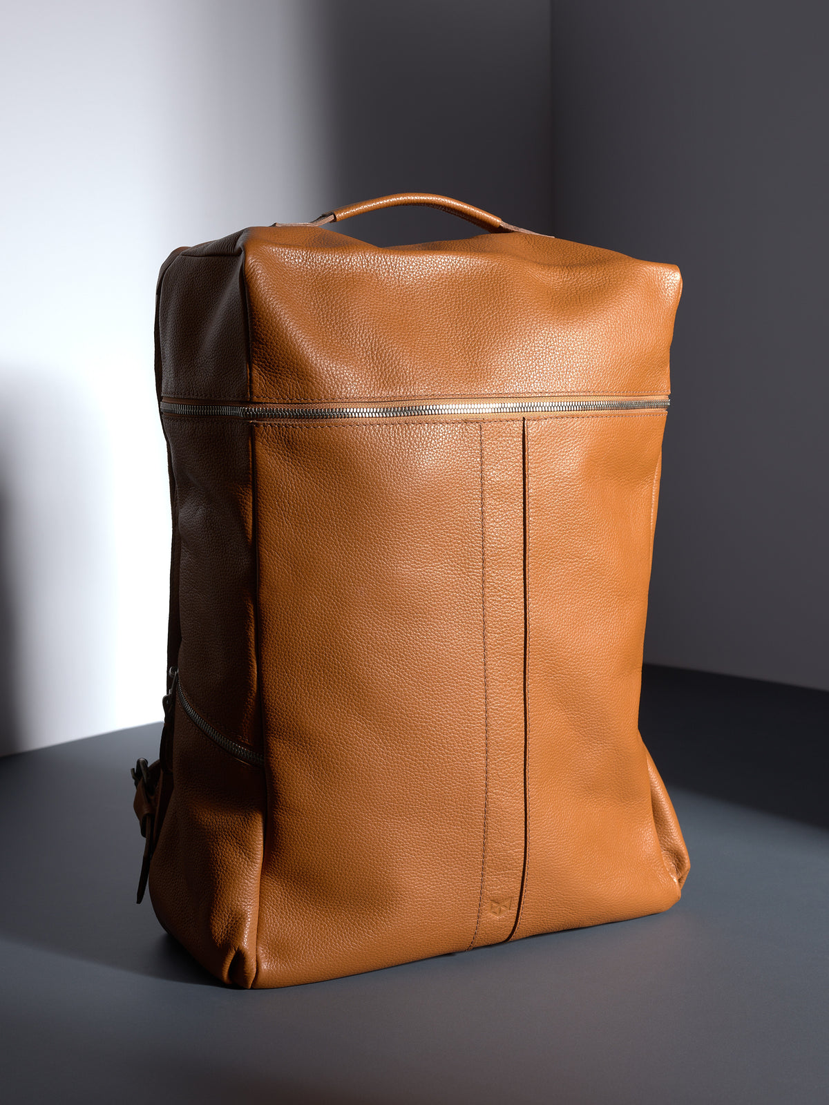 Front view of the full-grain tan leather Capra Banteng backpack with a pebbled texture and silver zippers.