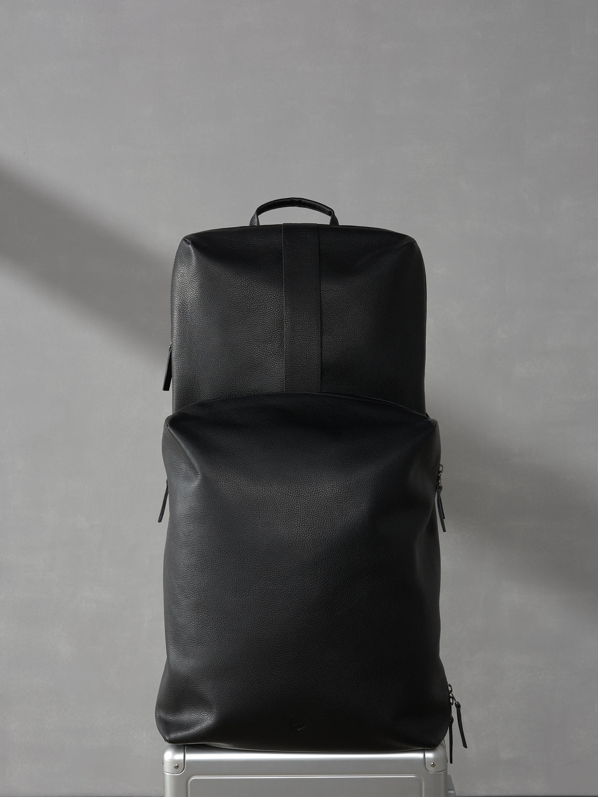 Elegant black leather travel backpack securely stacked on top of a premium silver rolling suitcase.