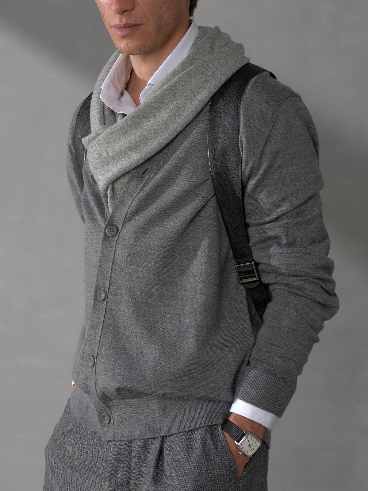 Close-up of a man in a grey cardigan wearing a black leather backpack strap with sleek metal hardware adjustment.