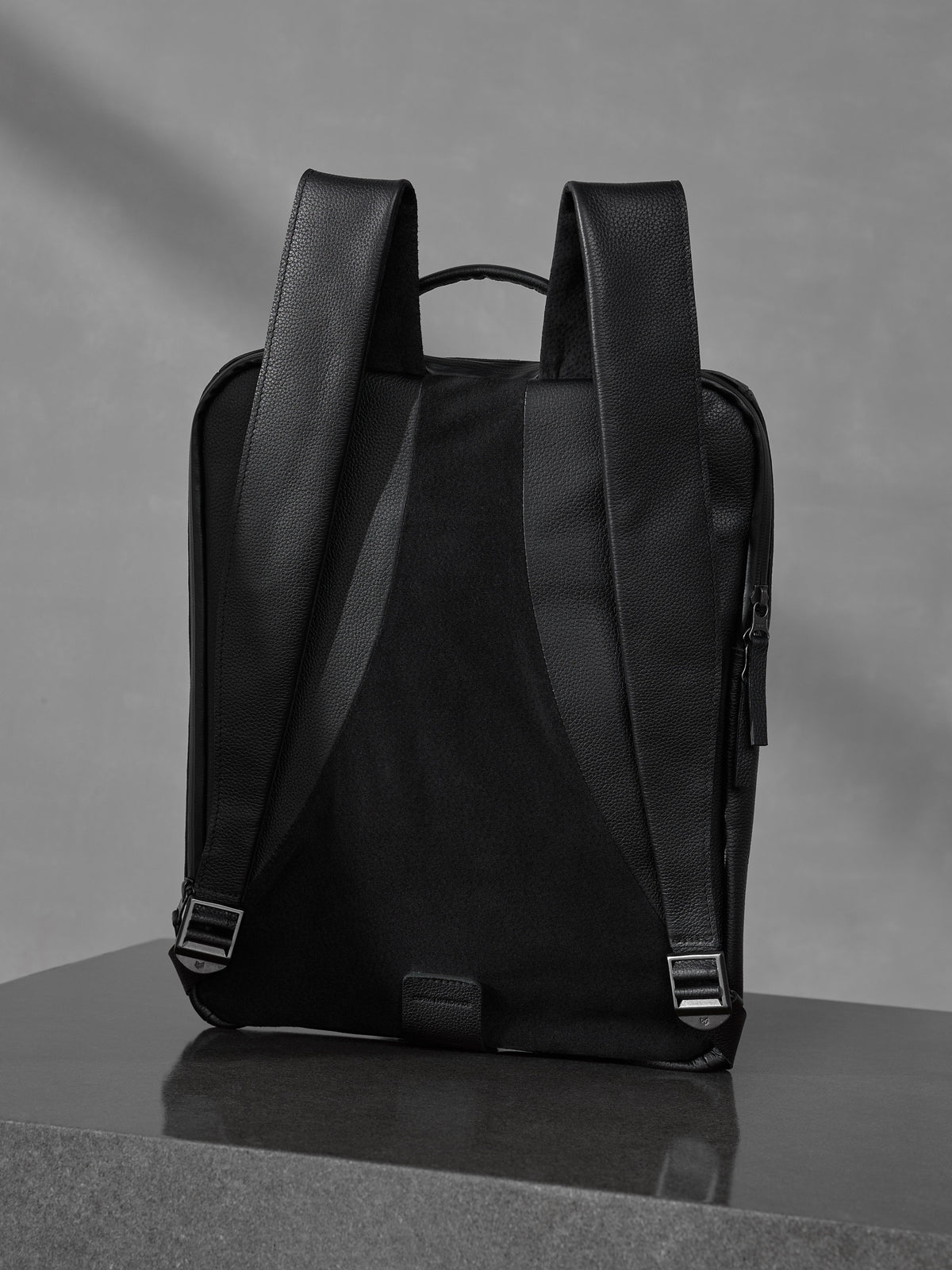 Rear view of a black full-grain leather backpack showcasing ergonomic shoulder straps and a breathable back panel.