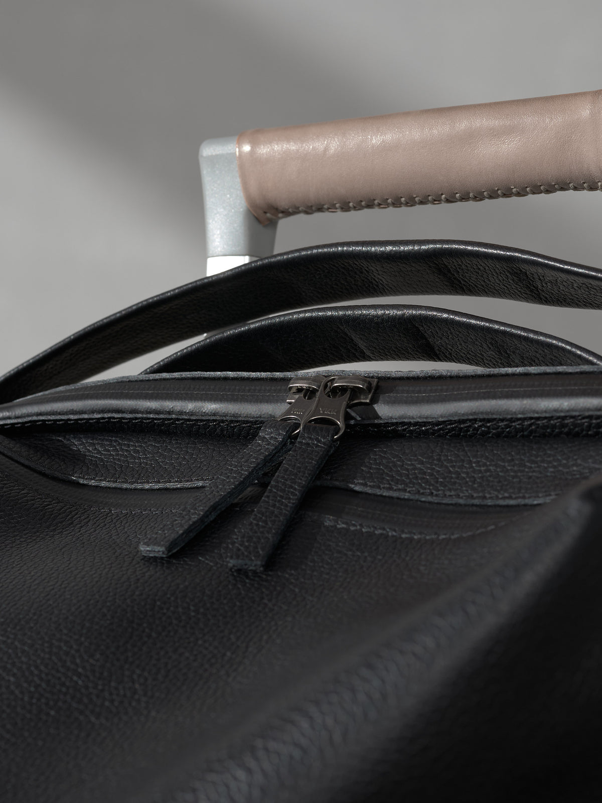 Macro detail of durable metal zippers and fine stitching on a black leather bag next to a tan leather handle.