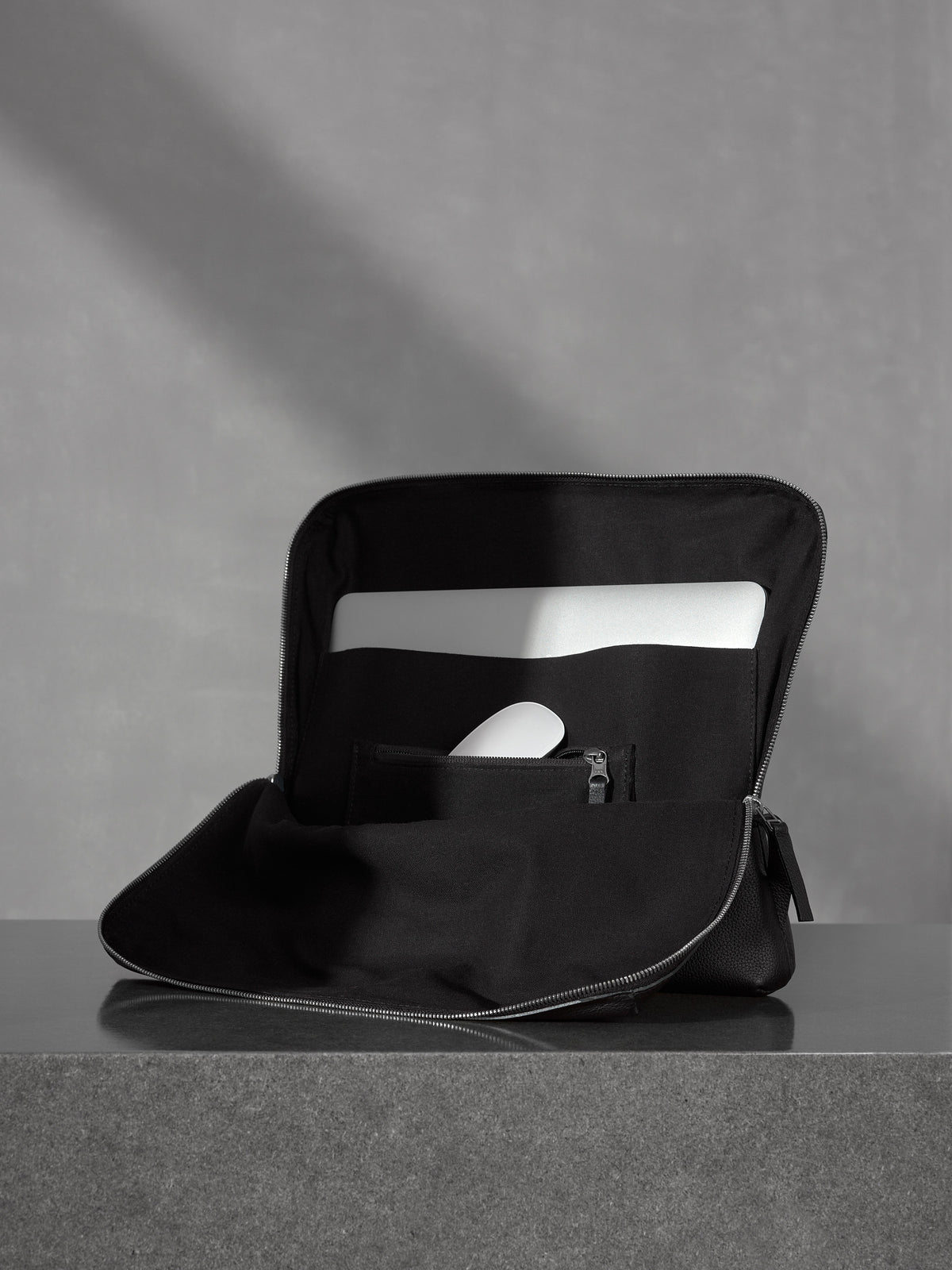 Open minimalist black leather tech organizer sleeve showcasing a laptop and a white mouse in a dedicated pocket.