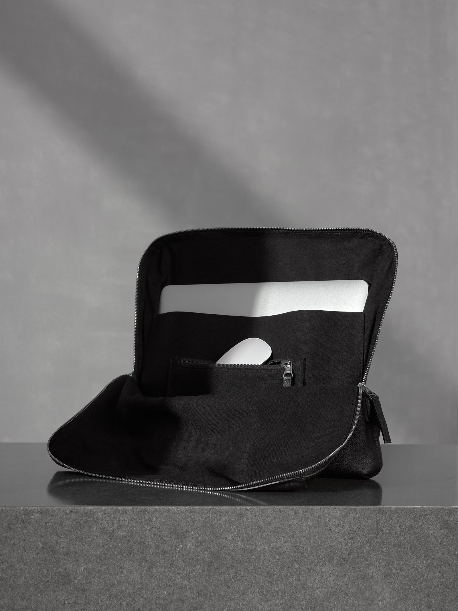 Open minimalist black leather tech organizer sleeve showcasing a laptop and a white mouse in a dedicated pocket.