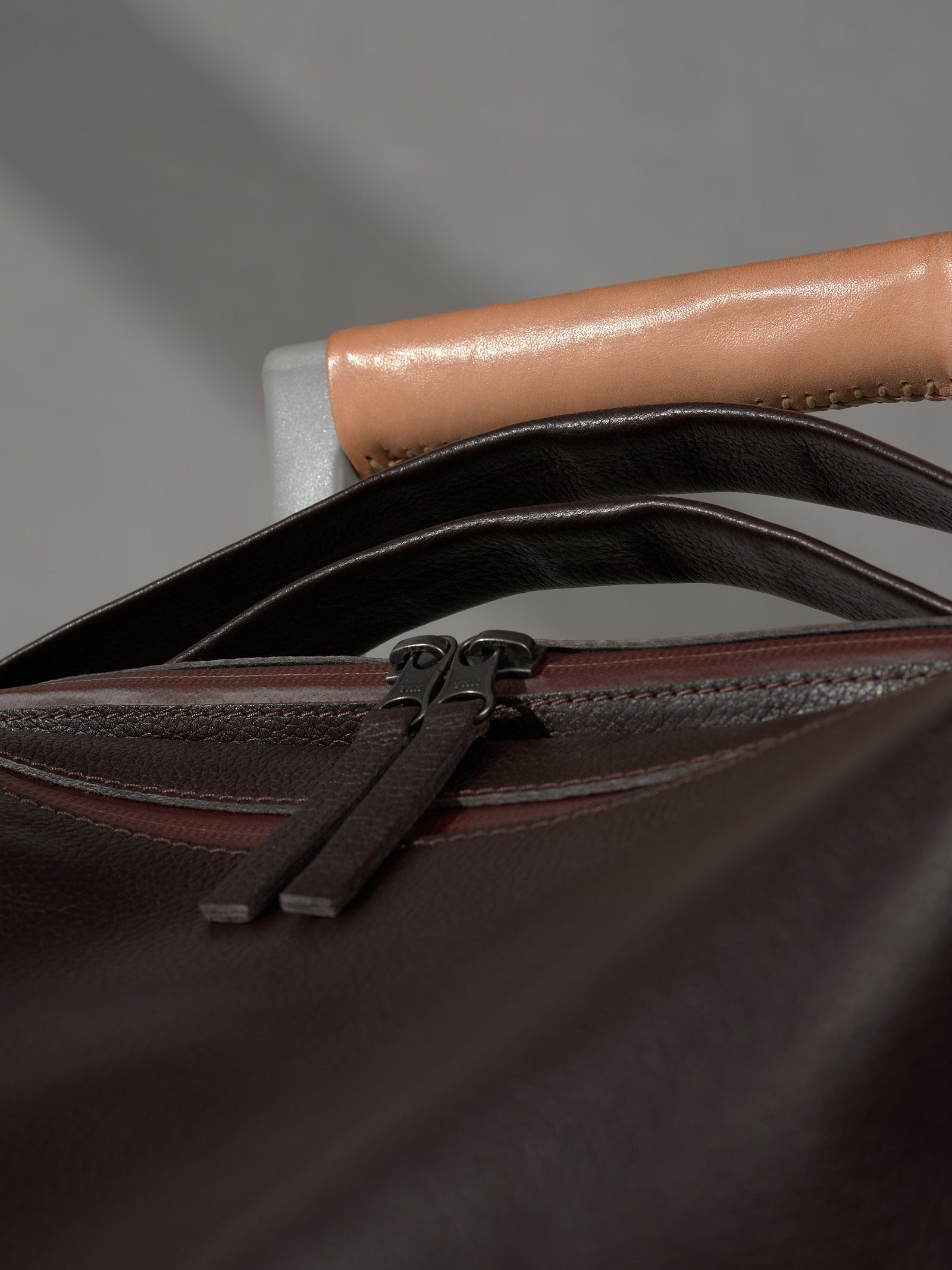 Detail shot of sturdy metal zippers on a luxury dark brown leather Capra Leather backpack.