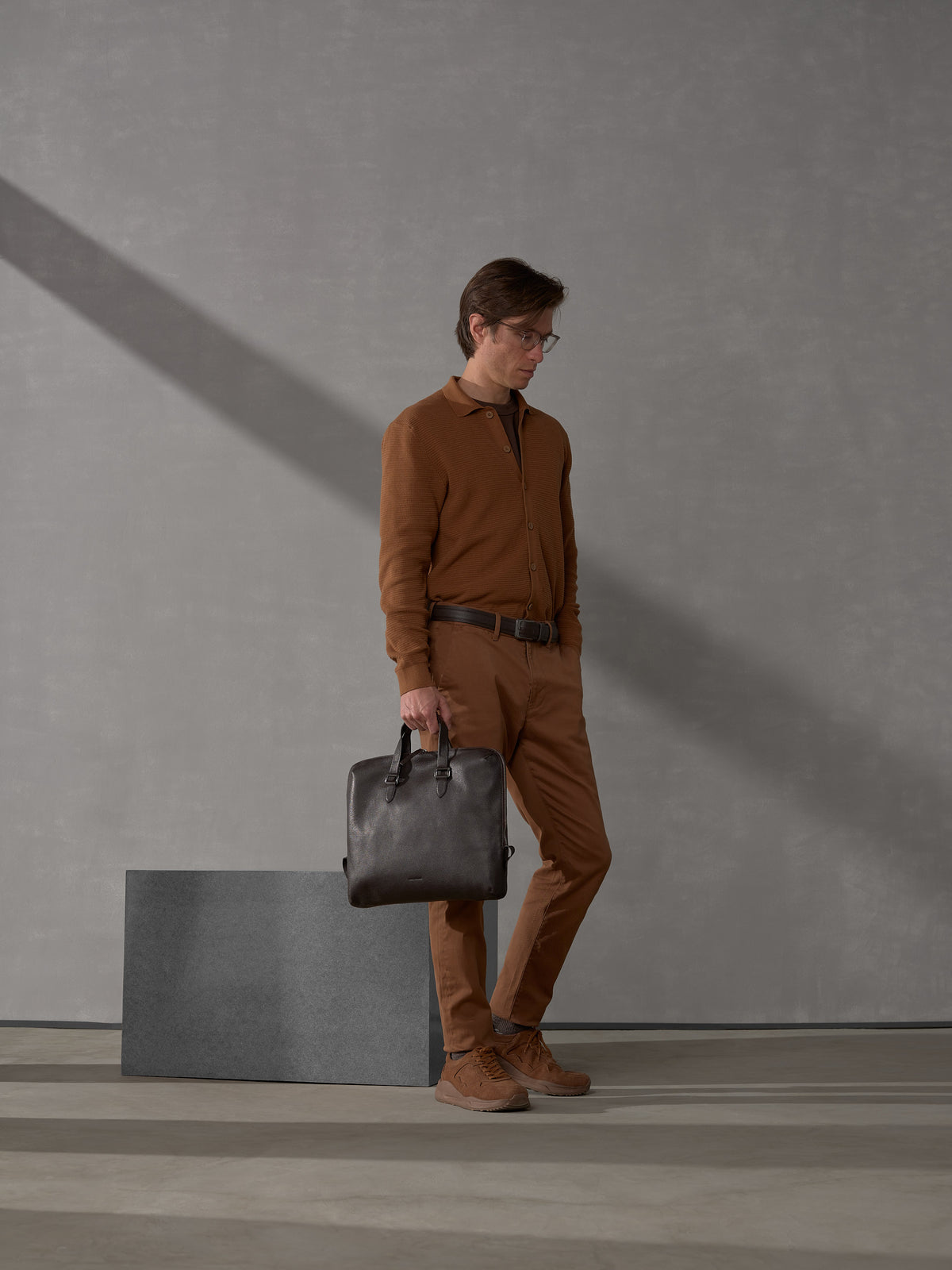Stylish man in monochromatic brown attire carrying a slim dark brown leather briefcase by Capra Leather.