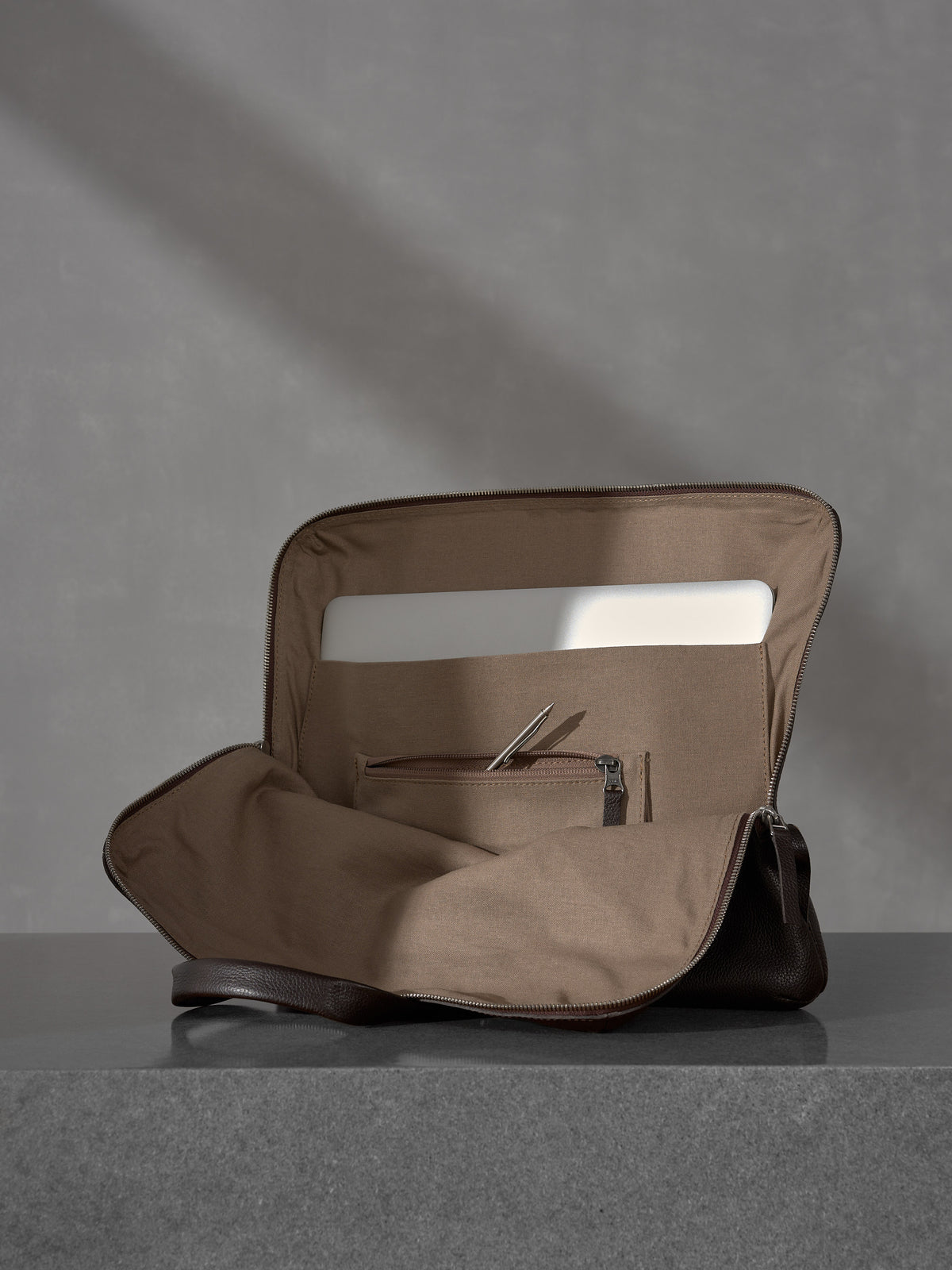 Open Capra Leather briefcase showing a laptop compartment and zippered pocket with a pen.