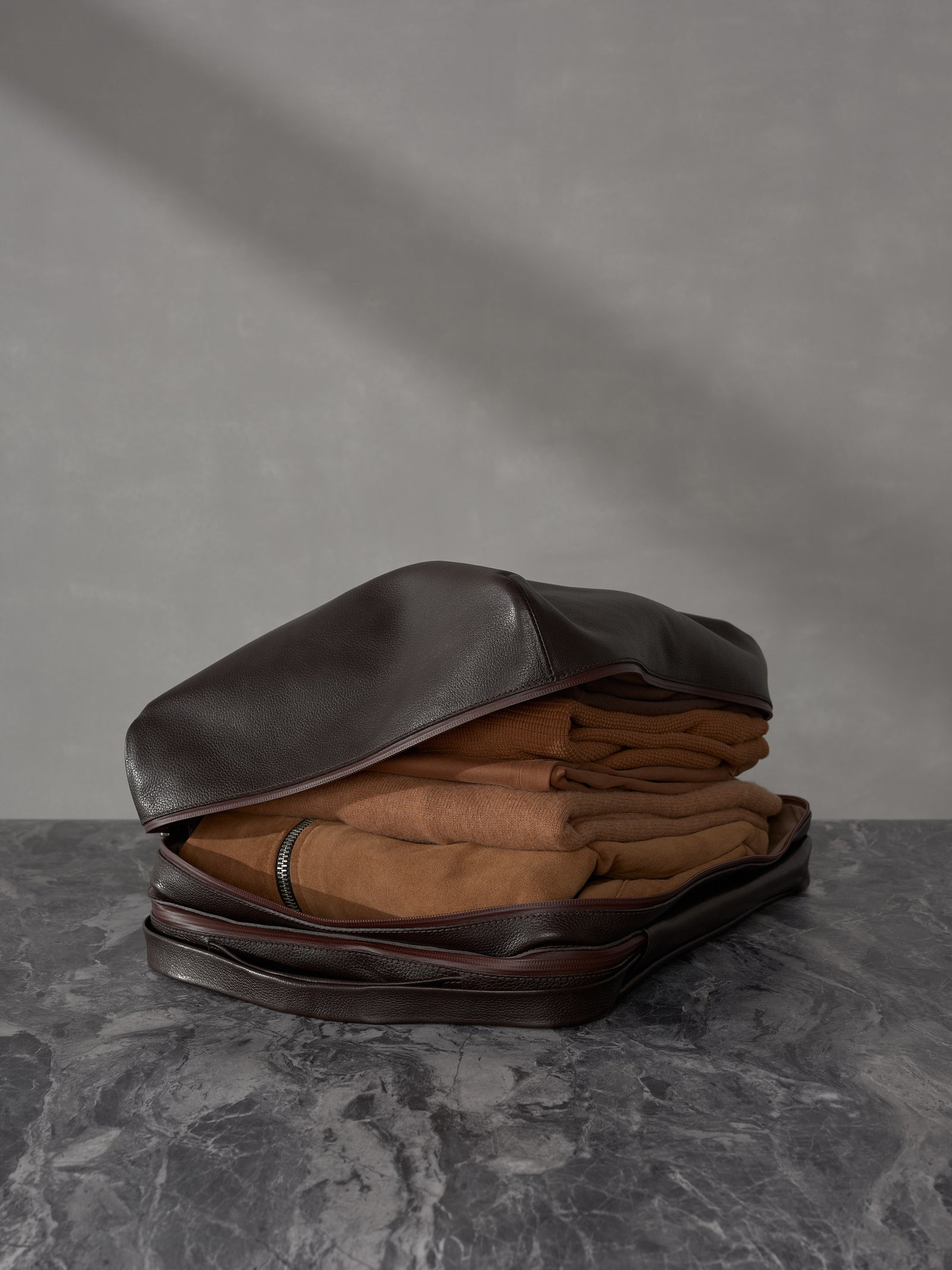 Man in brown stylish clothing standing with Capra Leather backpack attached to a silver rolling suitcase.