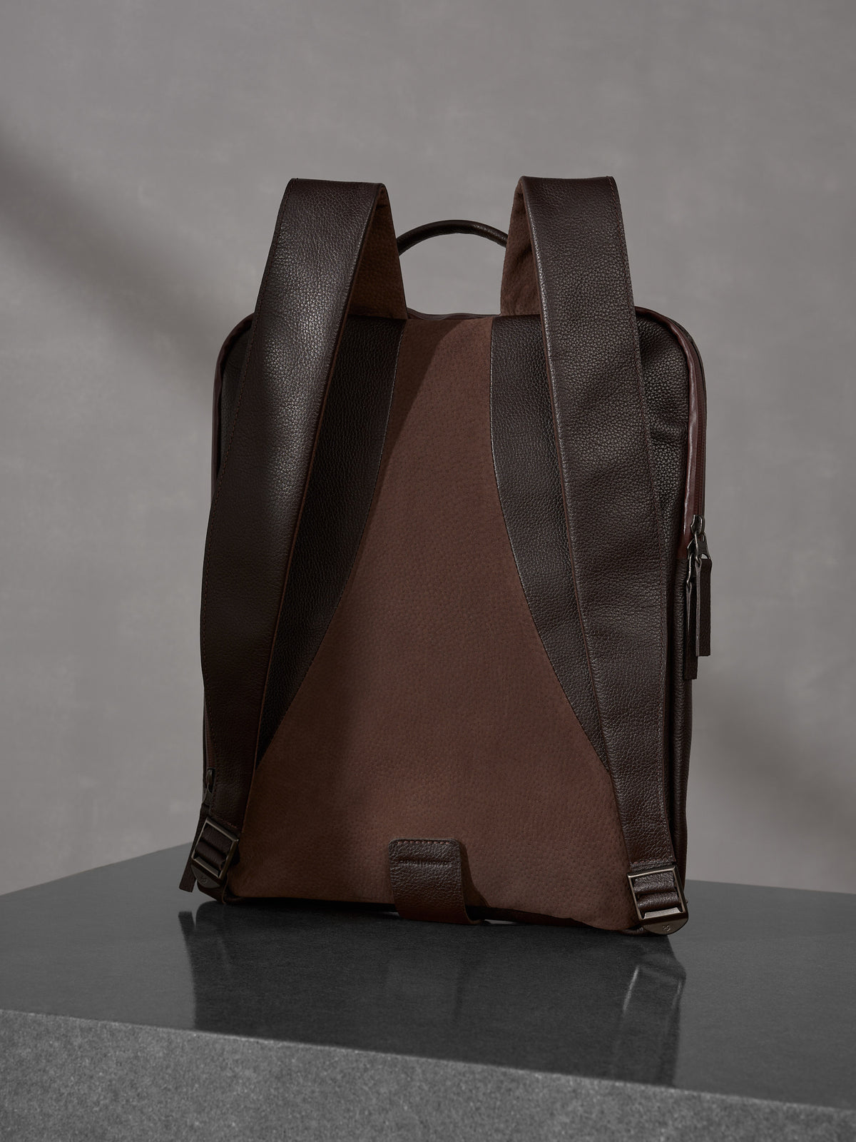 Rear view of a luxury dark brown Capra Leather backpack with ergonomic shoulder straps on a polished surface.
