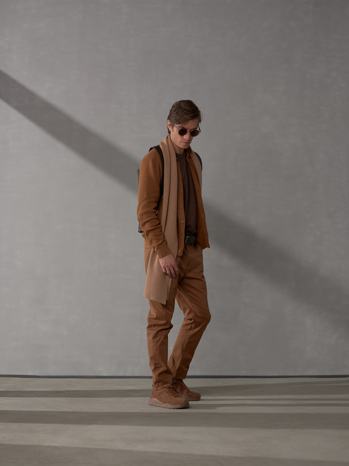 Full-body shot of a stylishly dressed man modeling a dark brown leather backpack by Capra Leather.