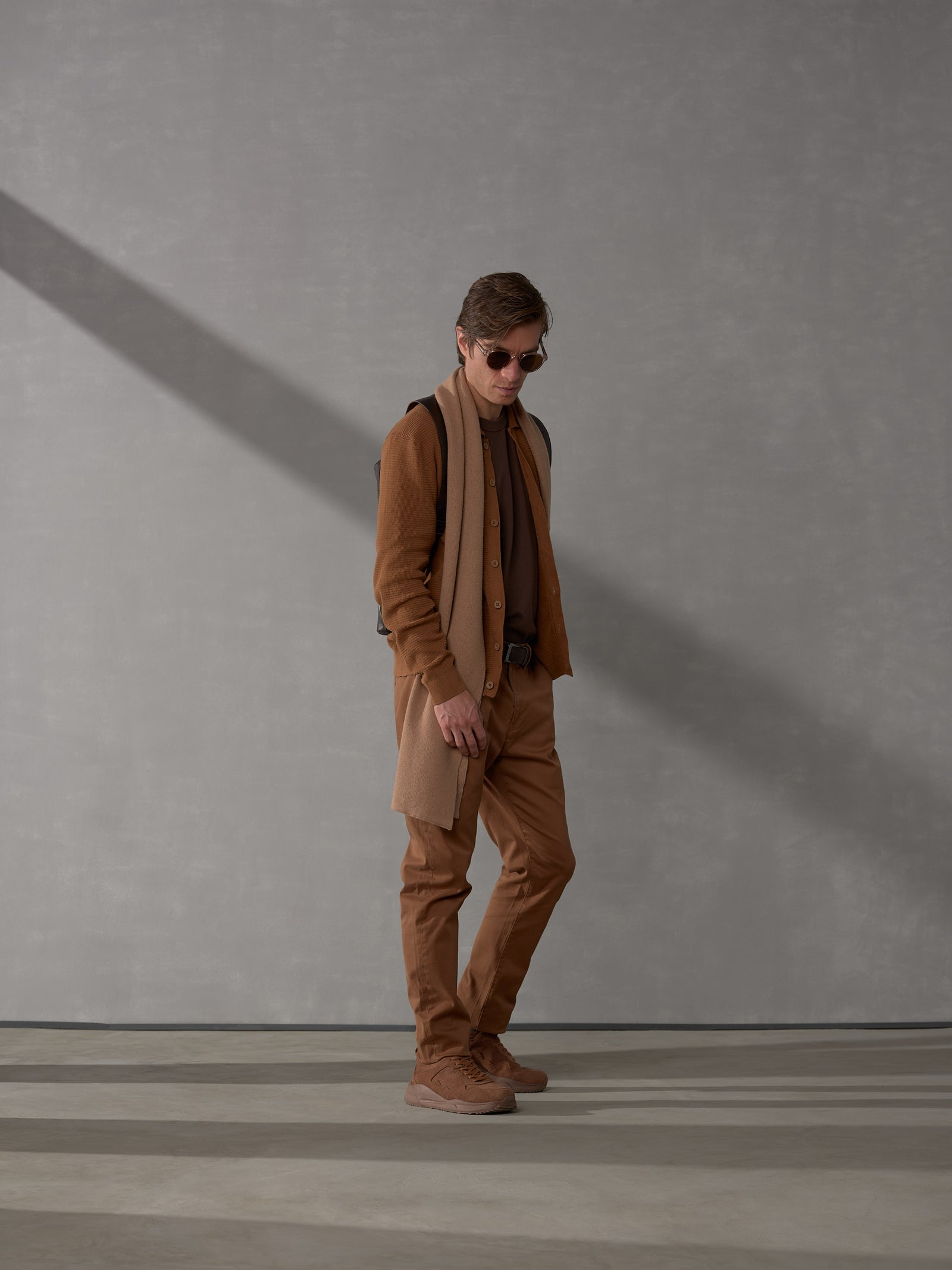 Full-body shot of a stylishly dressed man modeling a dark brown leather backpack by Capra Leather.