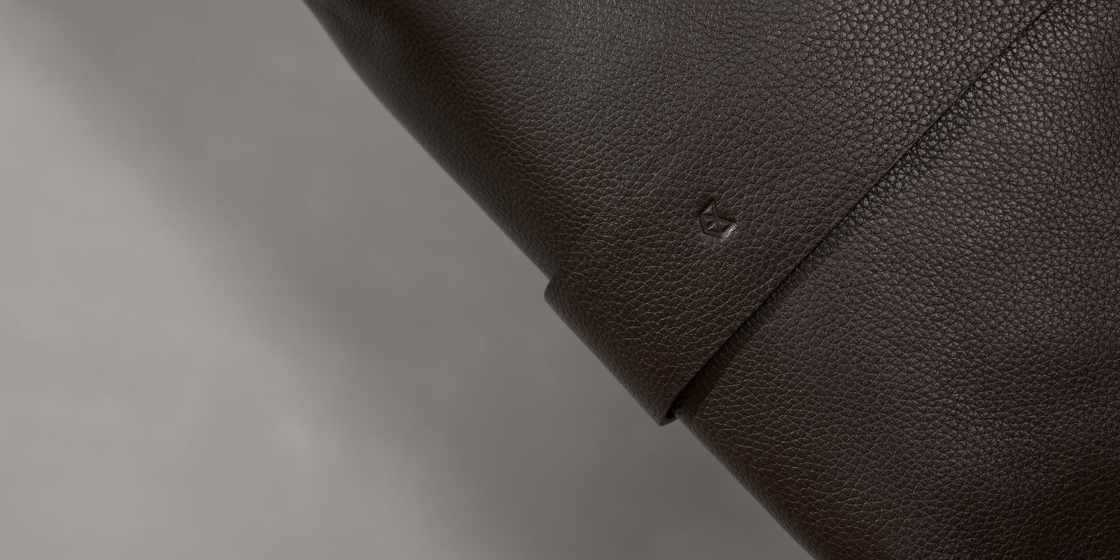 Close-up of a subtle, embossed geometric logo on a dark brown full-grain leather luggage strap.