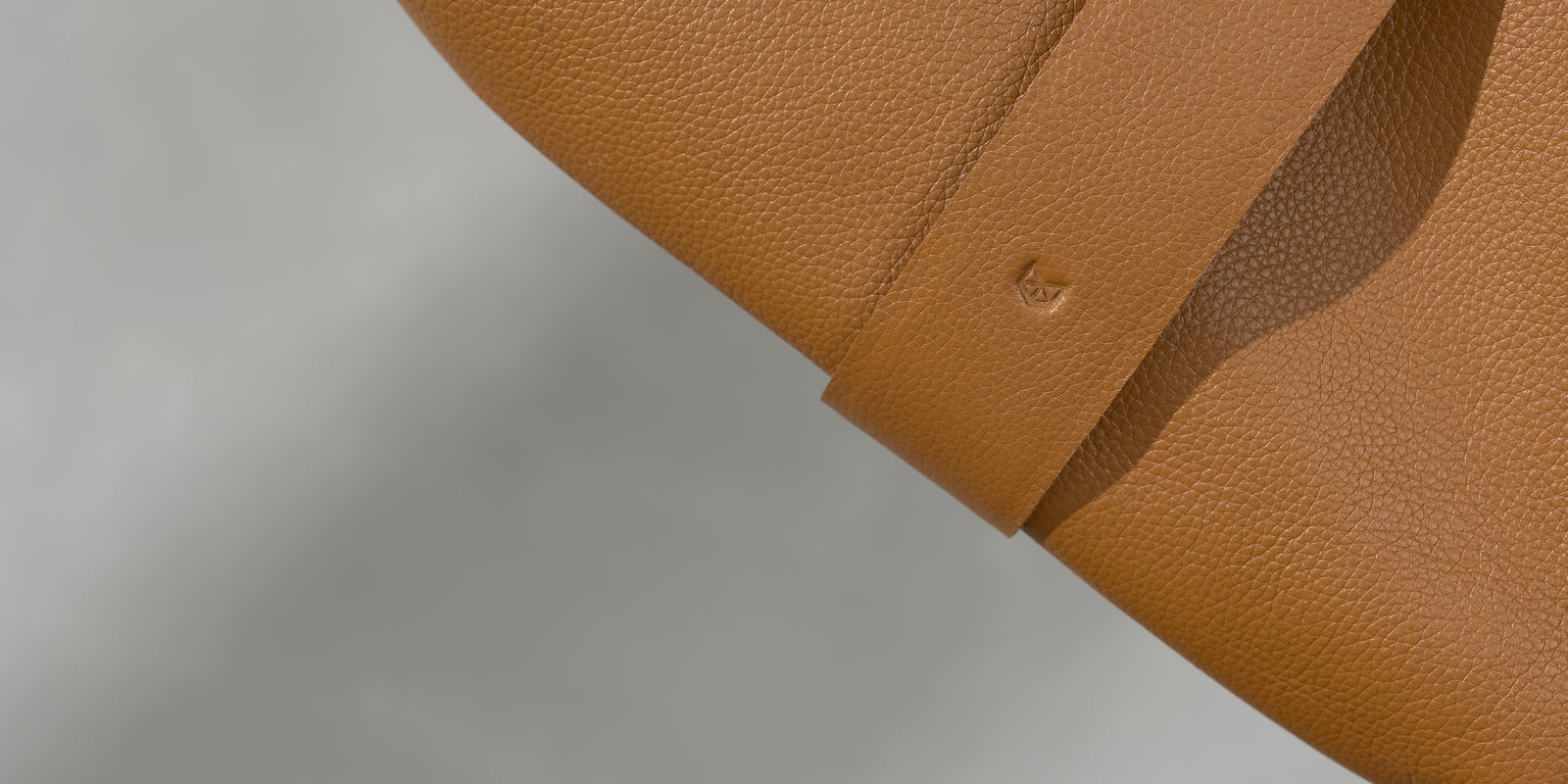 Close-up of the small, minimalist logo debossed on a wide tan leather strap.
