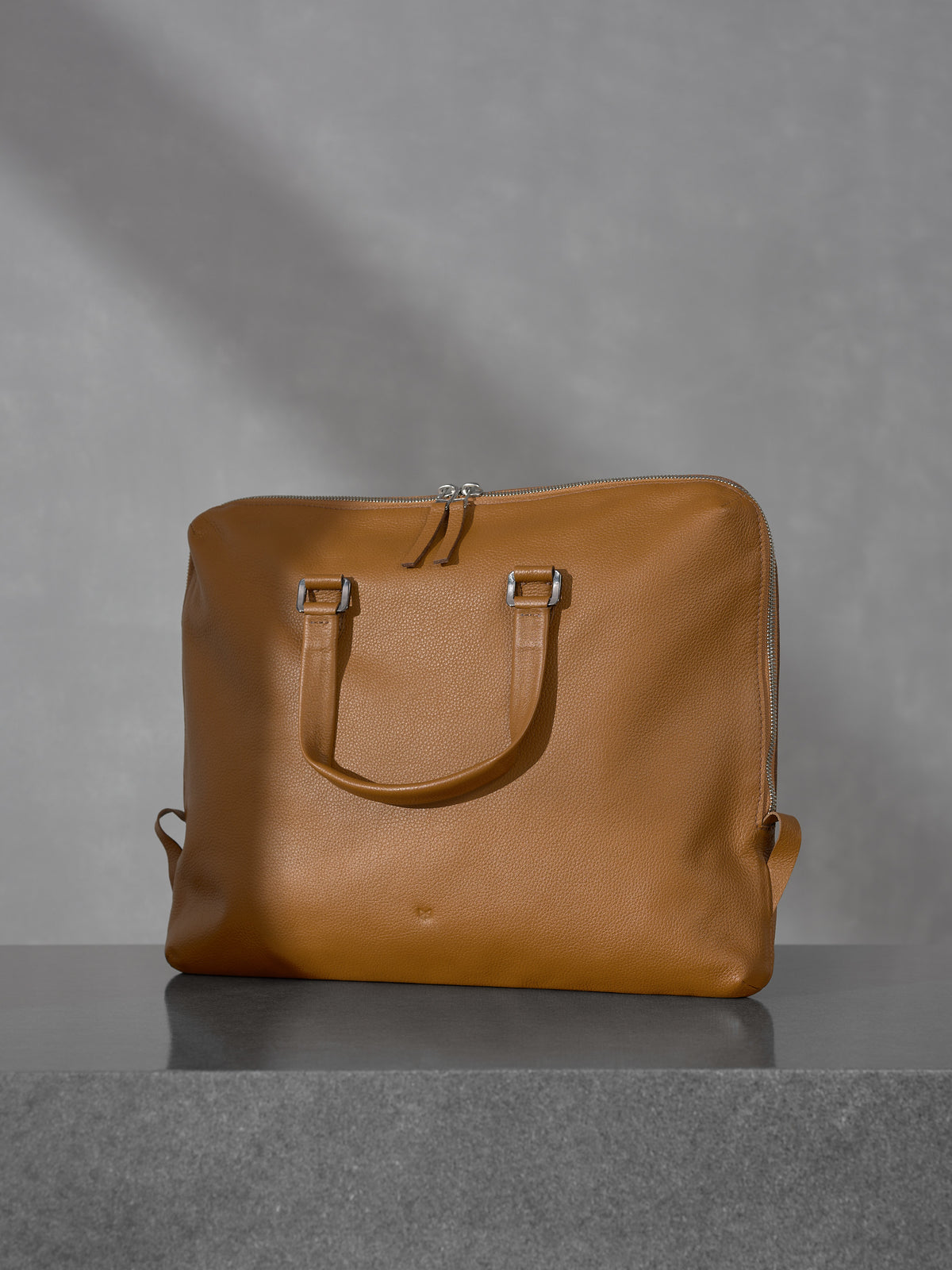 Front view of the minimalist tan leather briefcase and laptop bag from Capra Leather featuring top handles and a clean, elegant silhouette.