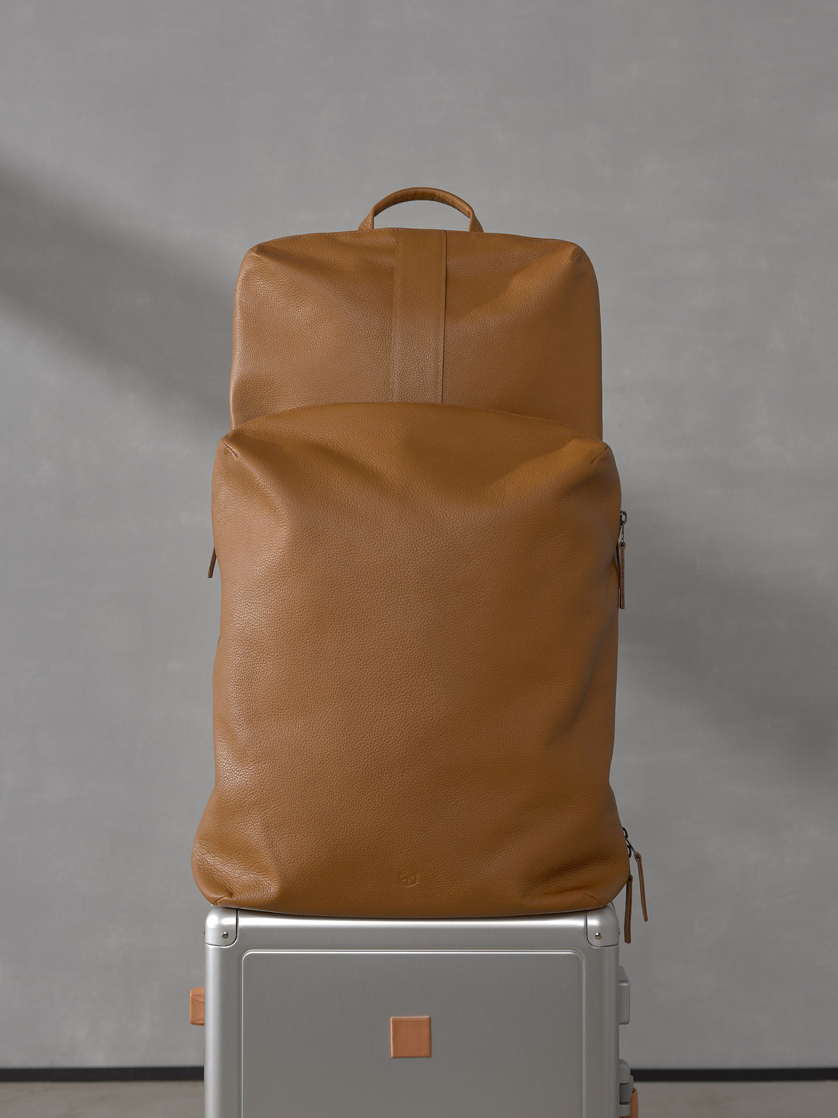 Front view of two modular tan full-grain leather bags from the Capra Leather Basalt system securely stacked on top of a silver rolling suitcase.