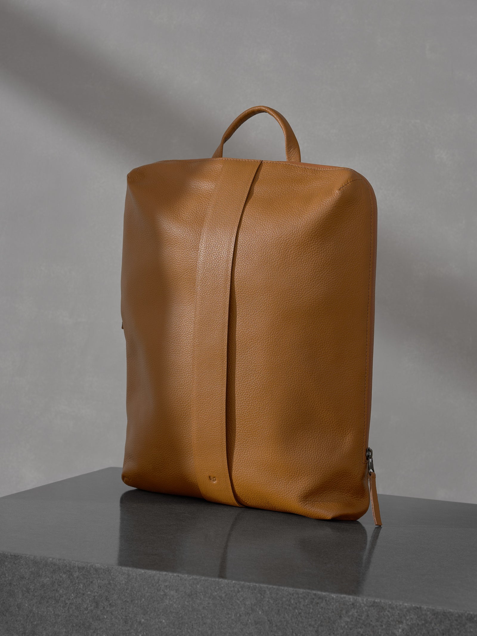 Open interior view of the Capra Leather tan backpack displaying its organized compartments containing a laptop, notebooks, and a black camera.