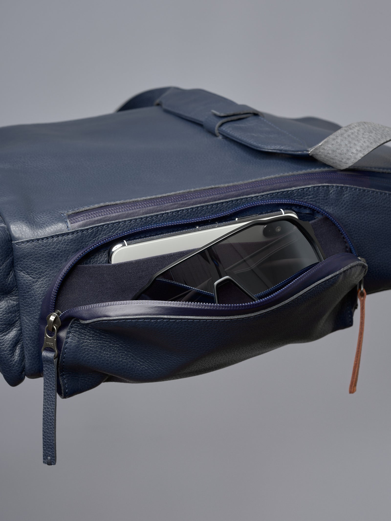 Blue leather bike bag's quick-access zippered pocket holding a smartphone and a pair of cycling glasses