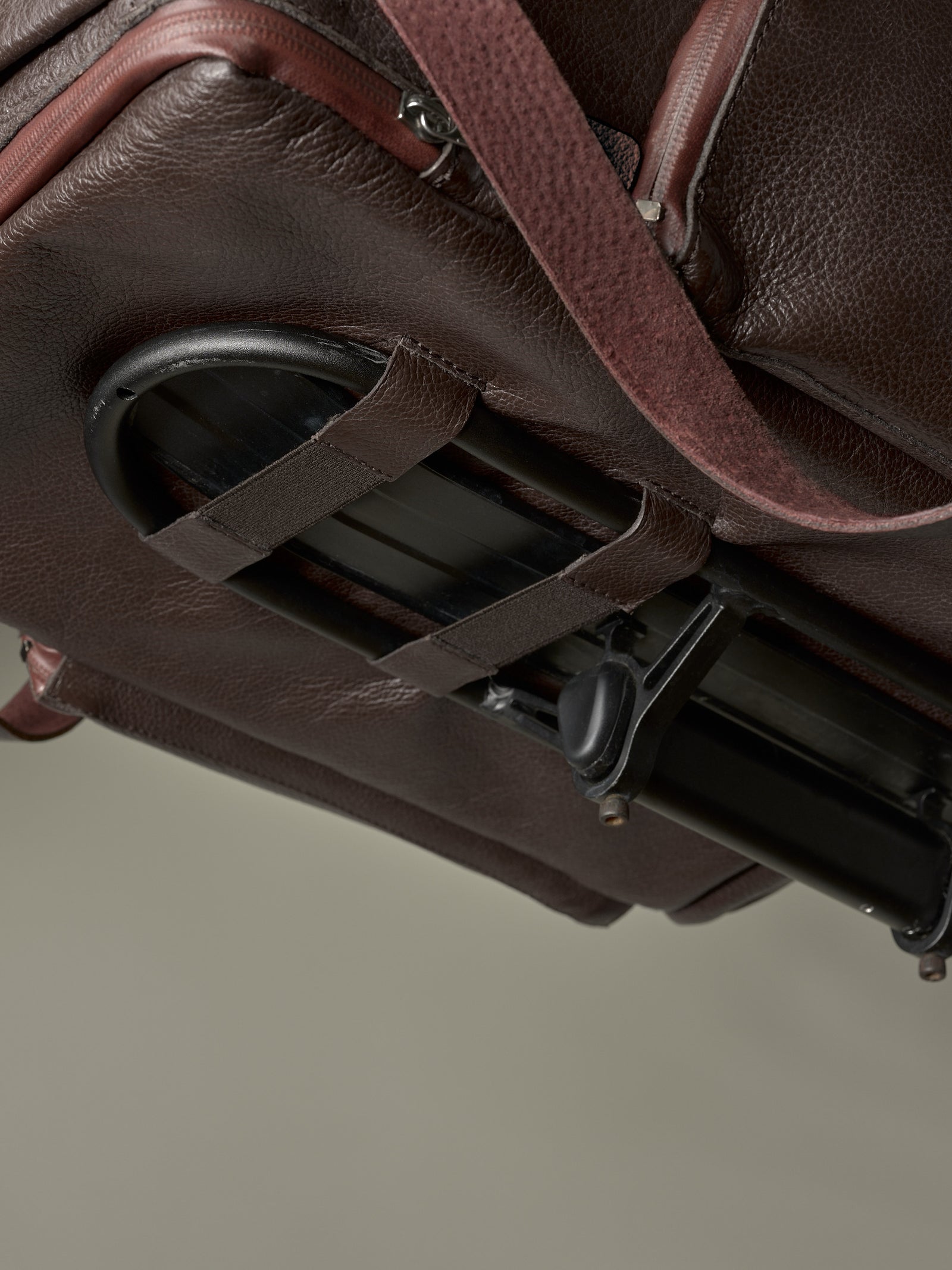 Underside of the brown leather bike bag showing the quick-release rack attachment system and leather securing straps.