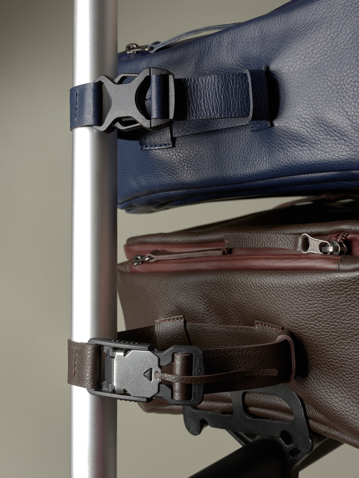 Vertical close-up showing the durable plastic buckle attachment straps on the blue and brown Capra Leather bike bags.